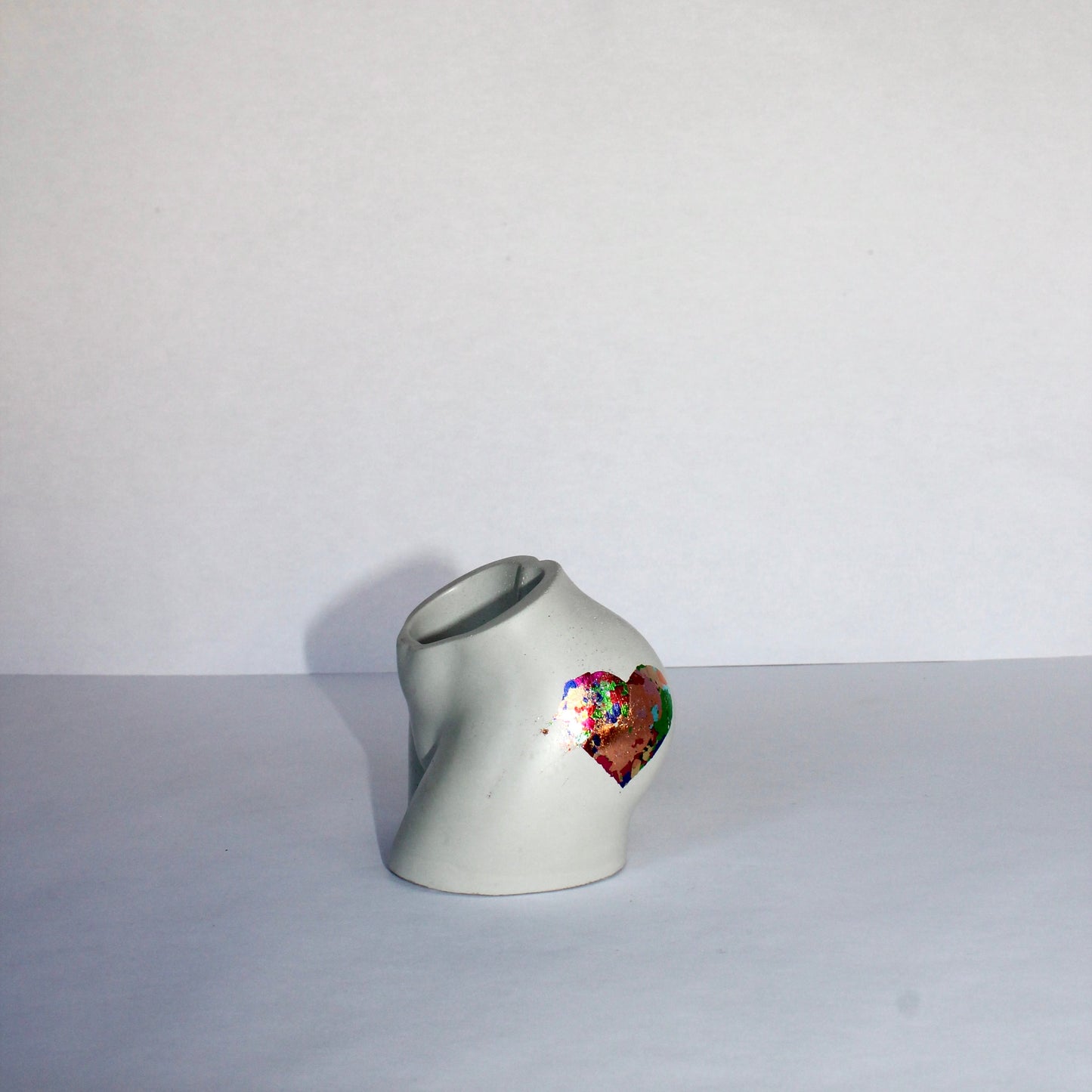 Small light gray body shaped vase with a colorful heart design on a white background