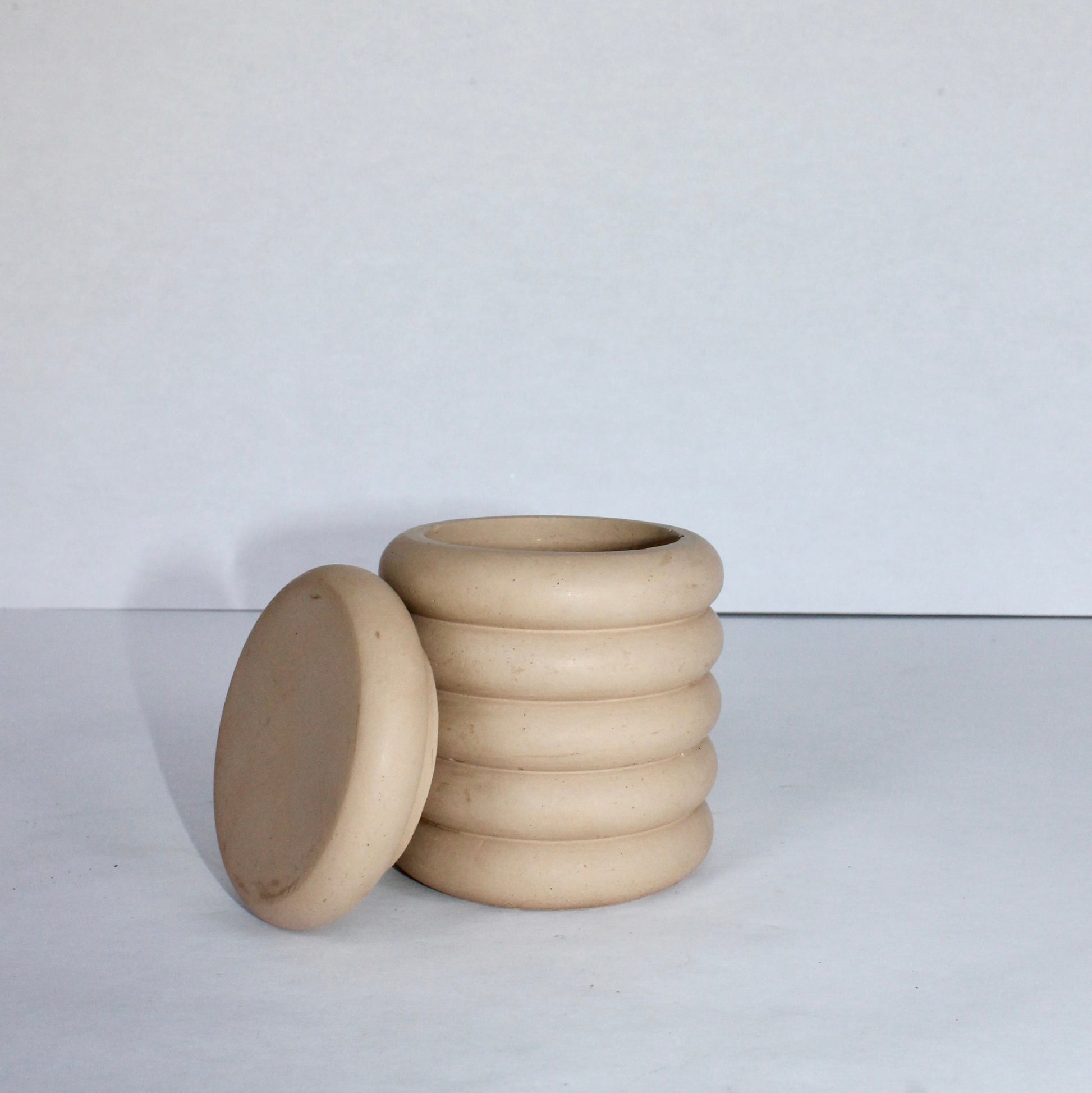 beige concrete jar with a lid propped on the side on a white background