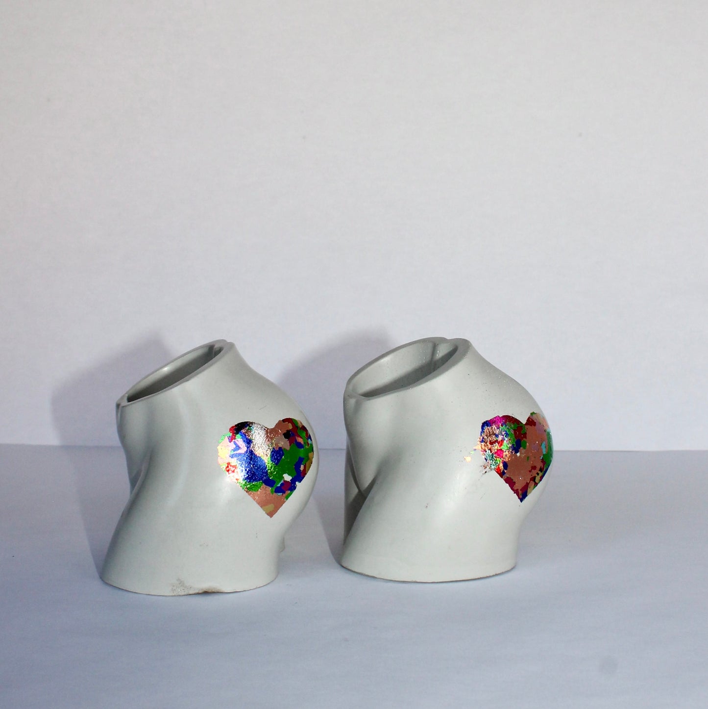 Two concrete bum shaped vases with colorful heart designs on a white background
