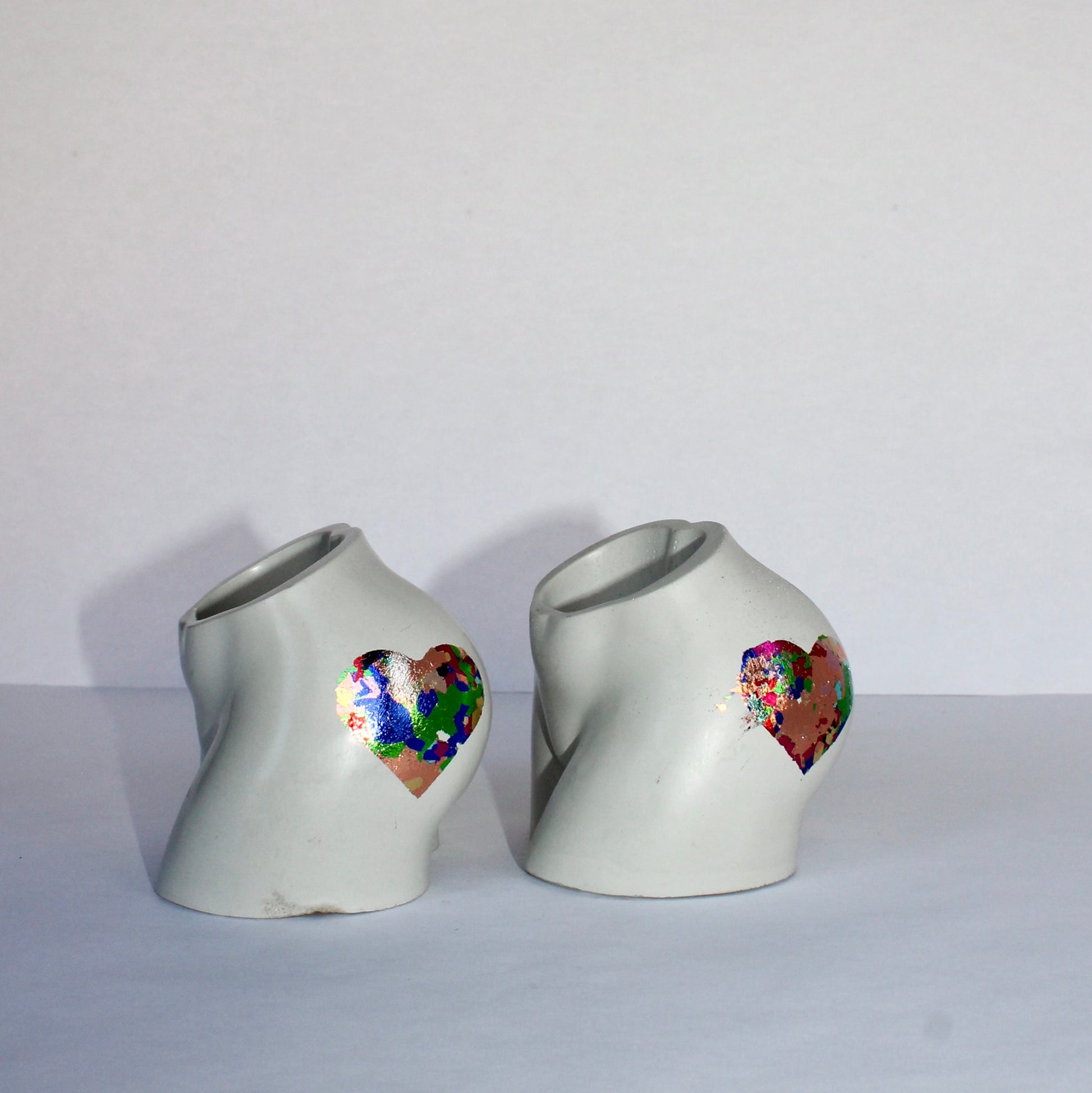 Two concrete bum shaped vases with colorful heart designs on a white background