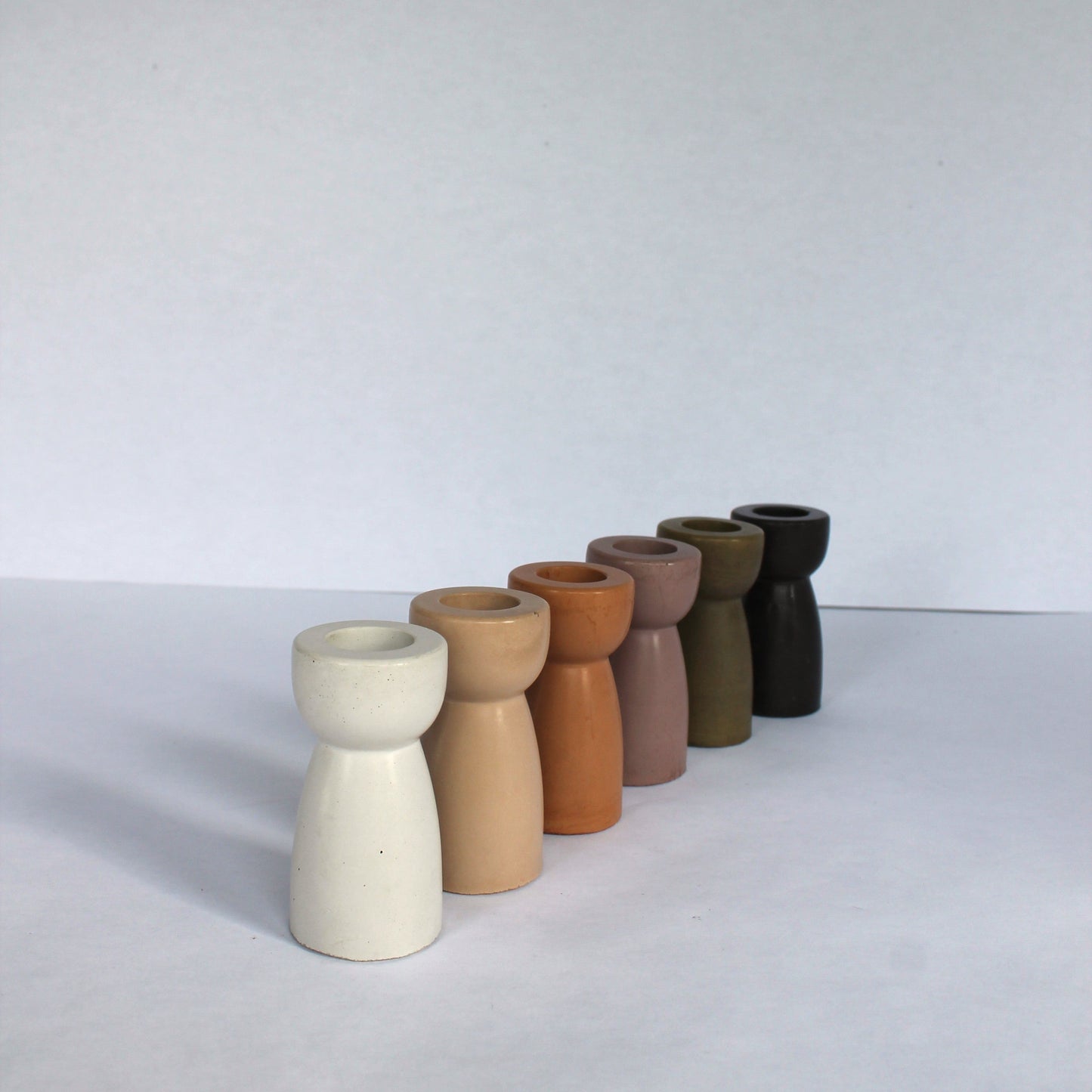 Six concrete candle stick holders in various earthy tones on a white background