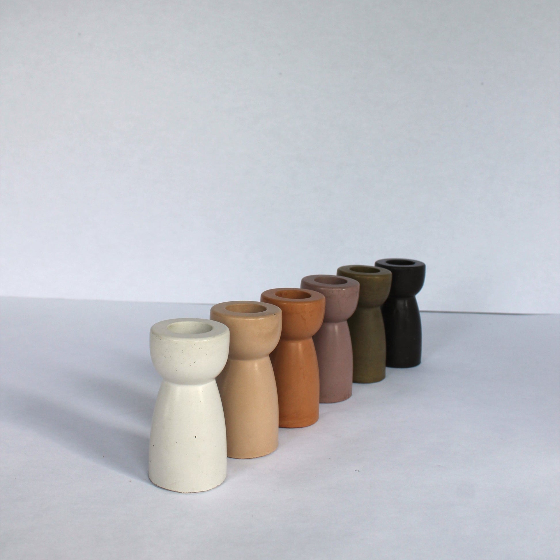 Six concrete candle stick holders in various earthy tones on a white background