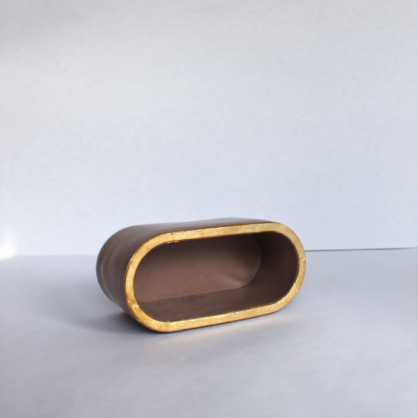 concrete oval dish on its side with gold rim on a white surface