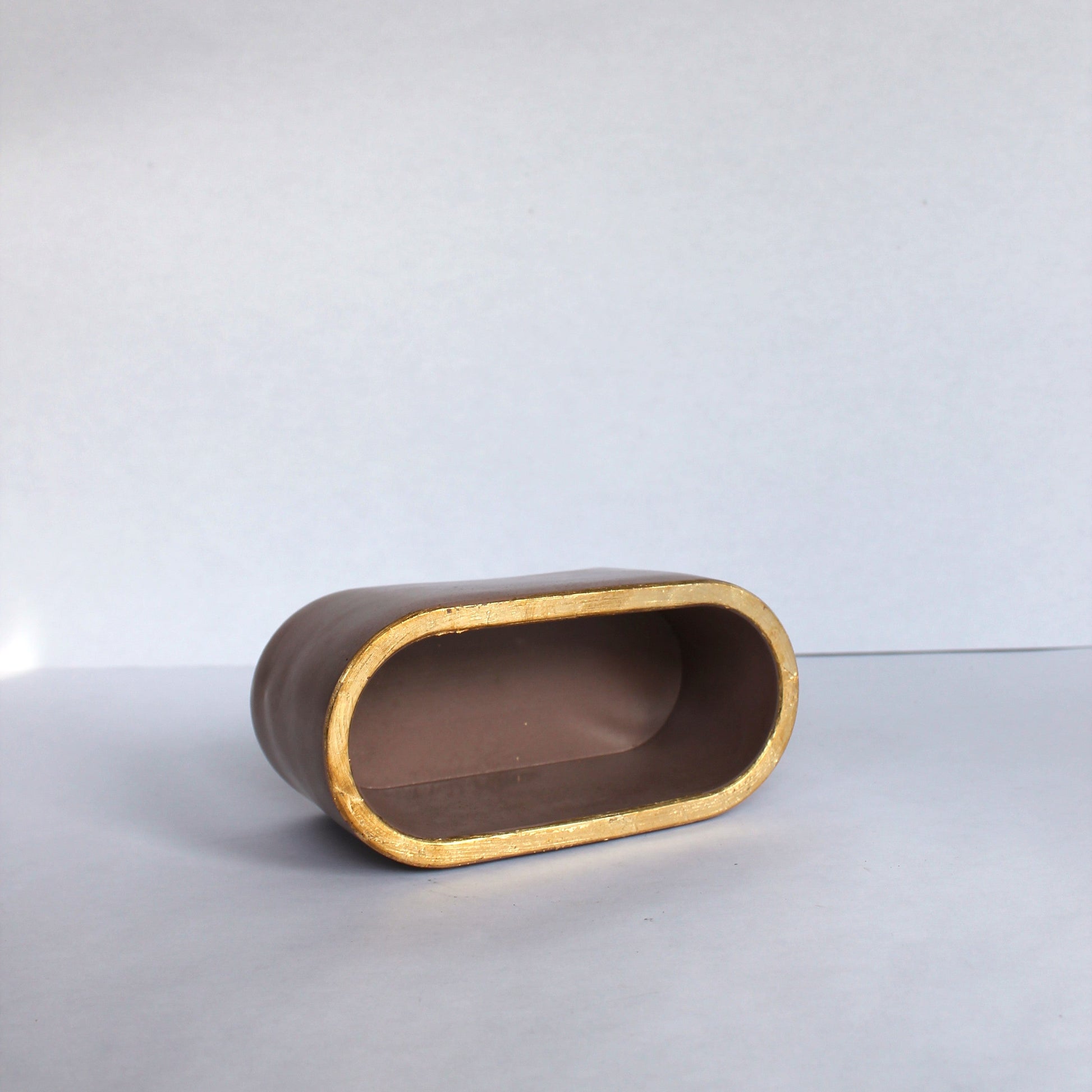 concrete oval dish on its side with gold rim on a white surface