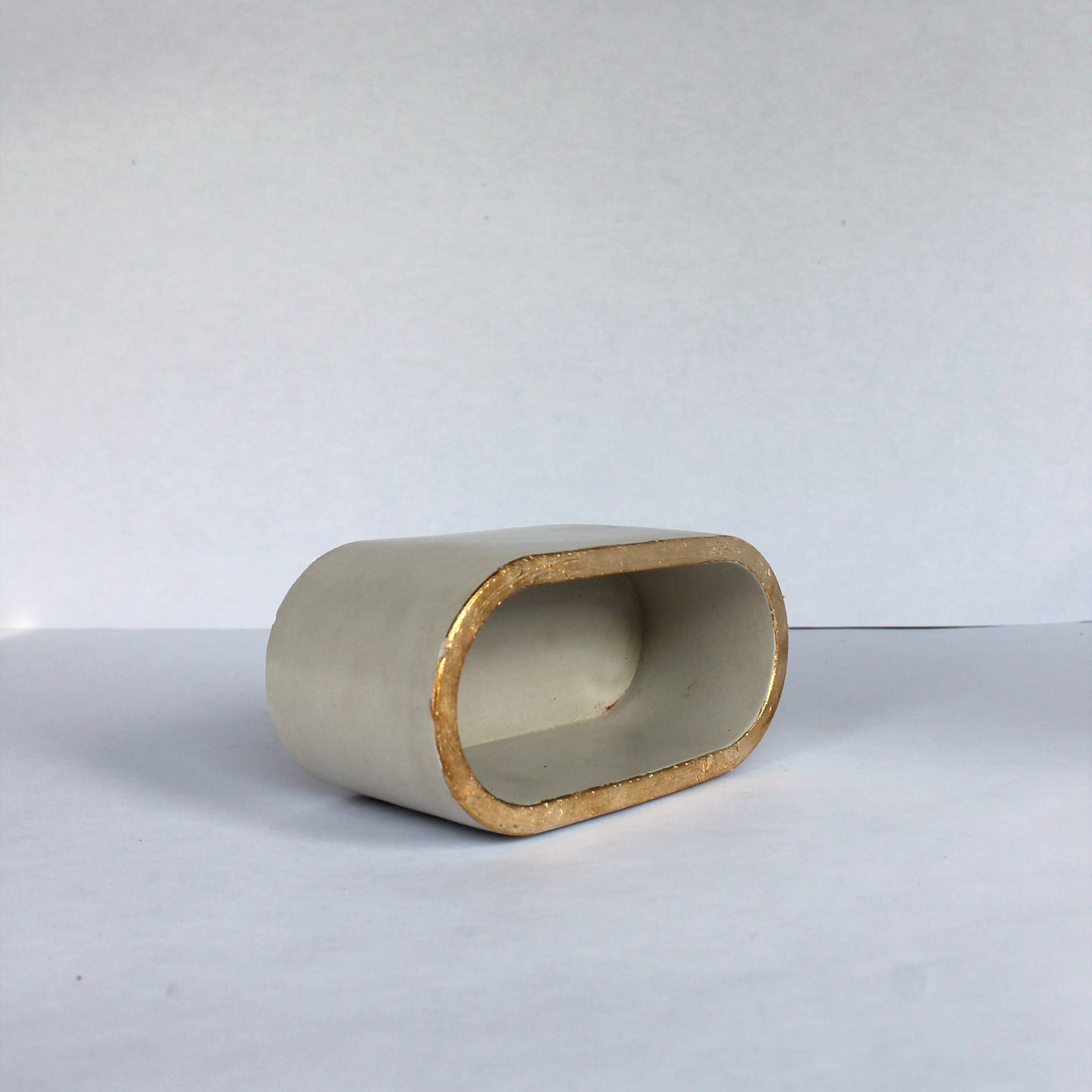 Cylindrical ceramic object with gold rim on a white background