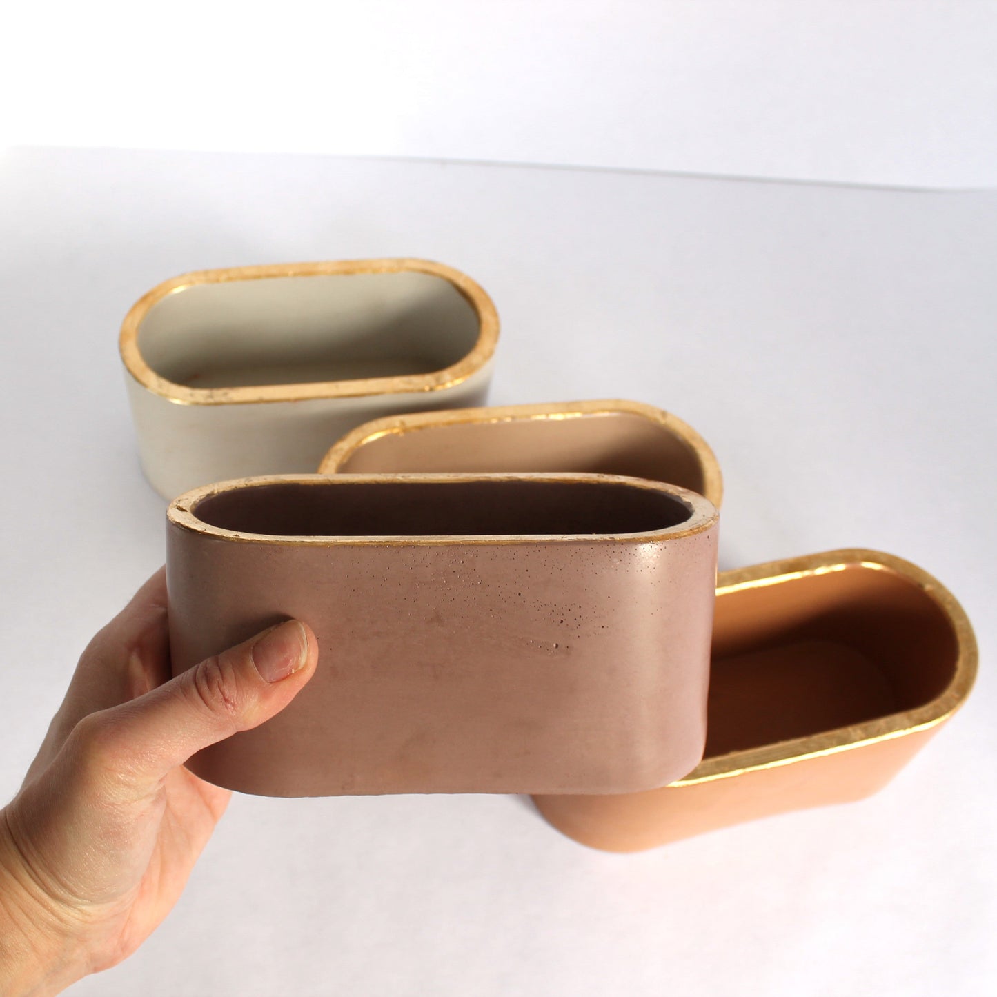 Hand holding a concrete container with other similar containers on a white surface