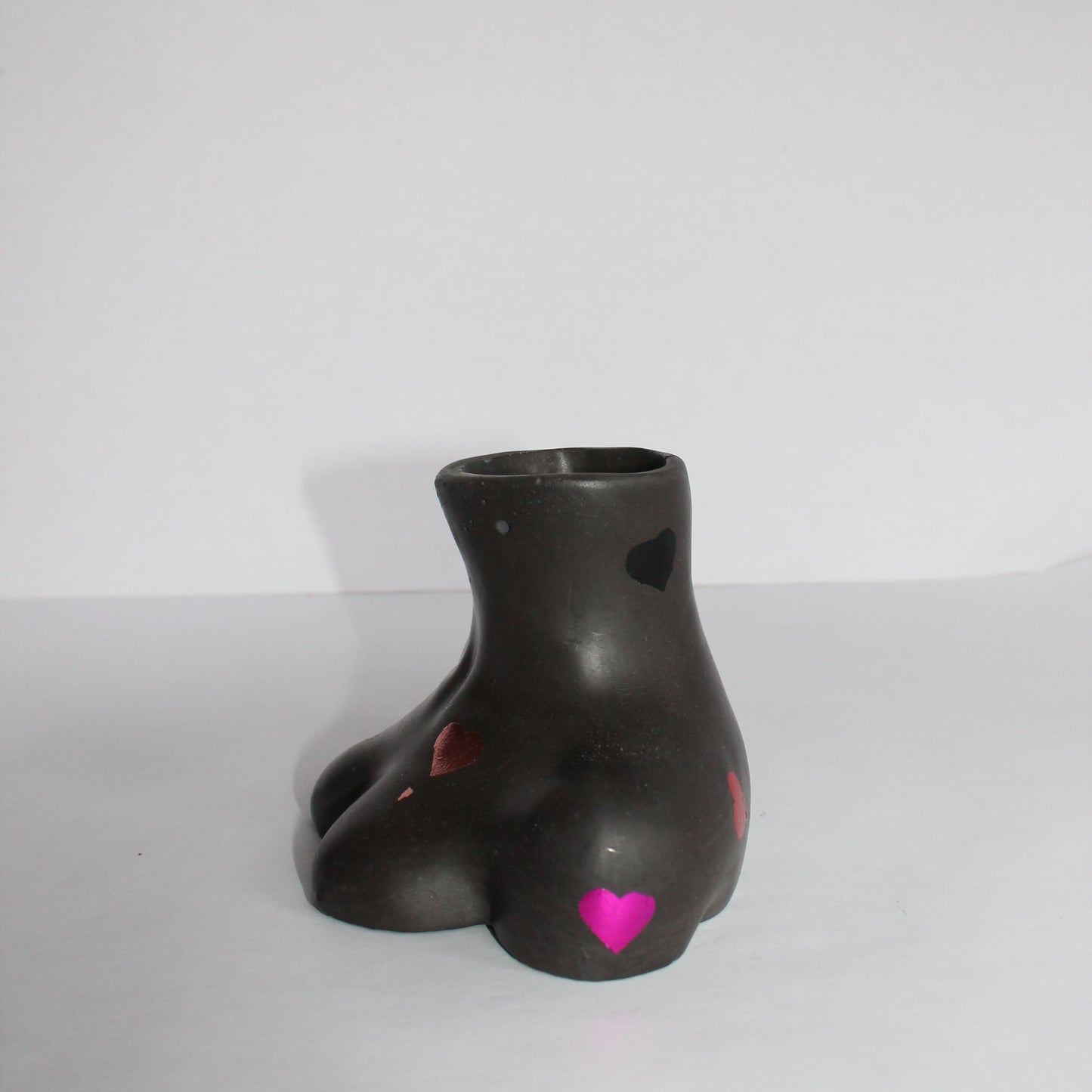 Black breast shaped vase with colored hearts on a white background
