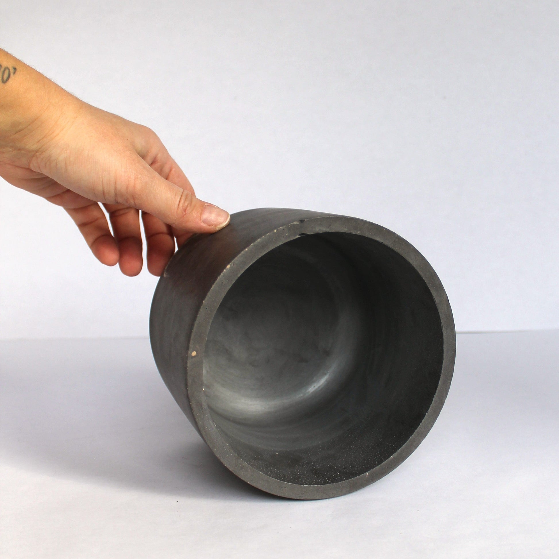 Hand holding a dark gray concrete pot on a white background