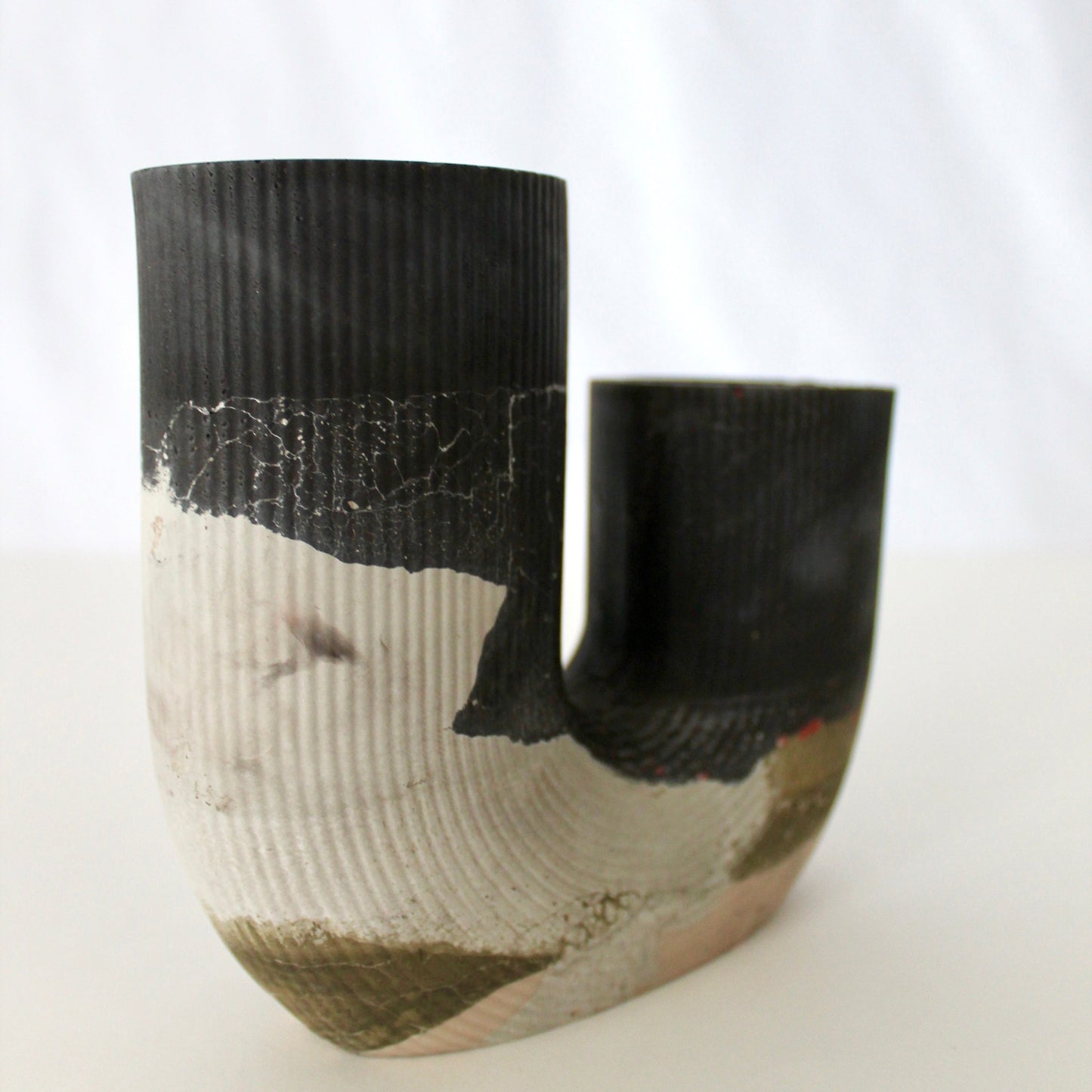 Multicolored concrete vase with black and green patterns on a white background