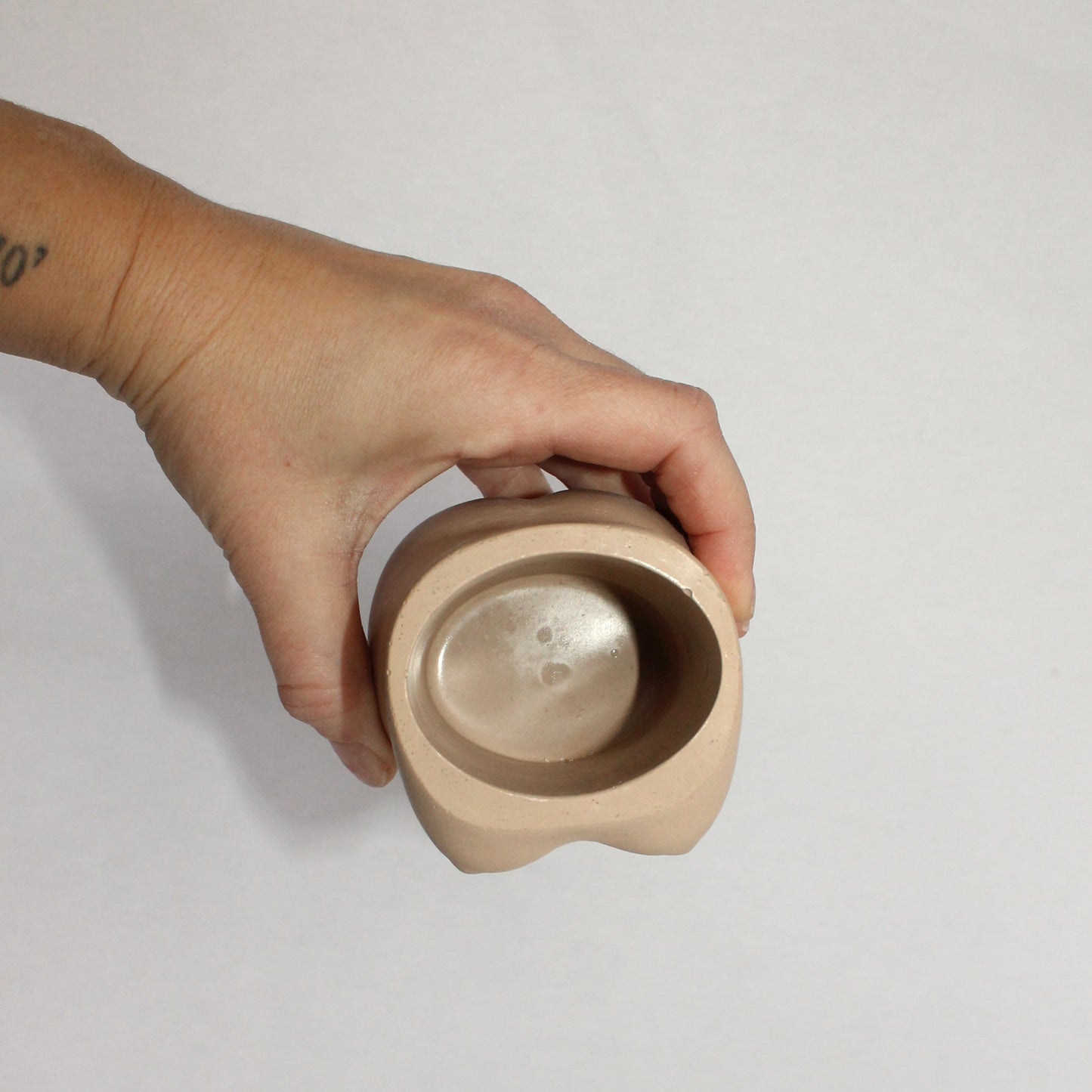 Hand holding a small concrete container against a white background