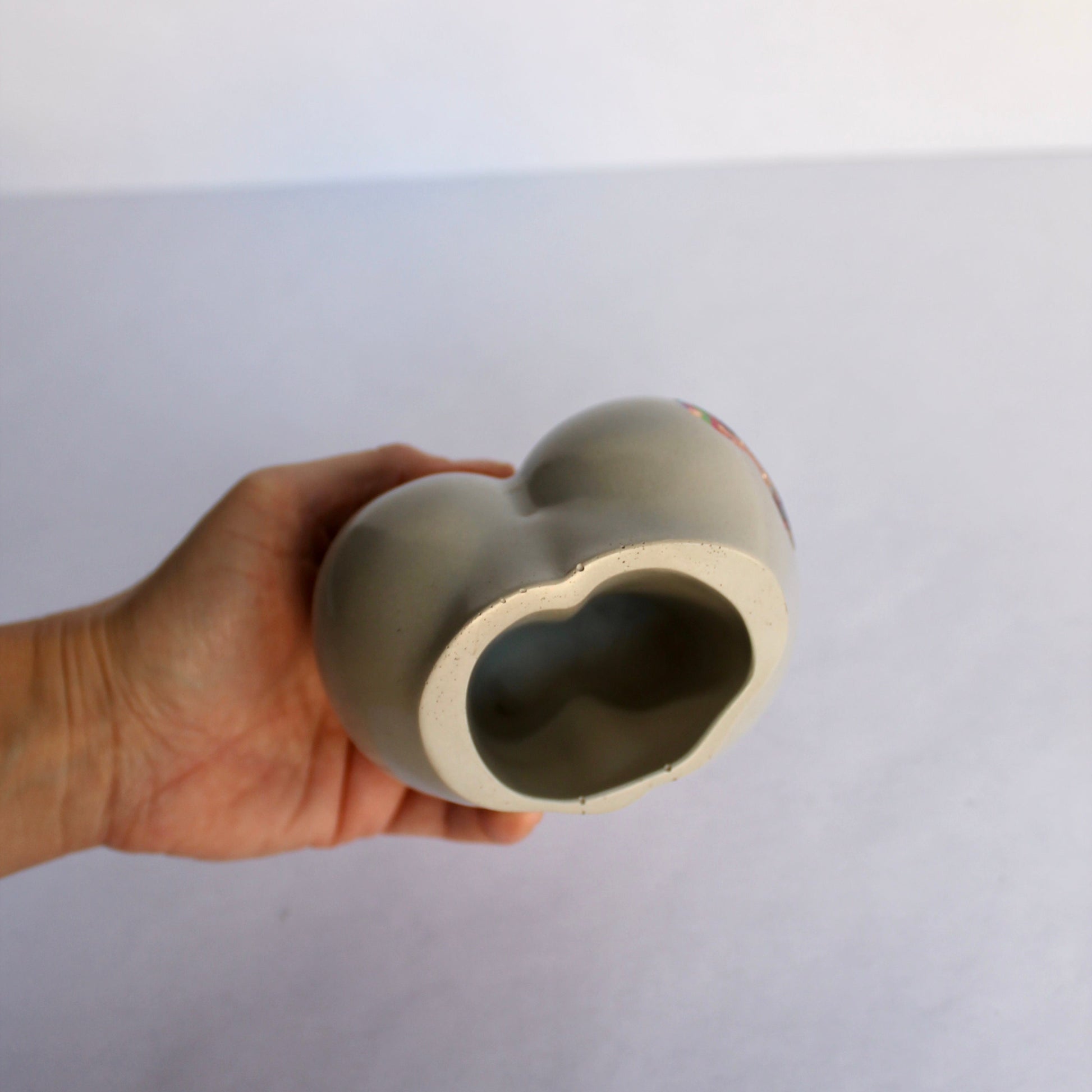 Hand holding a ceramic female body-shaped object against a white background