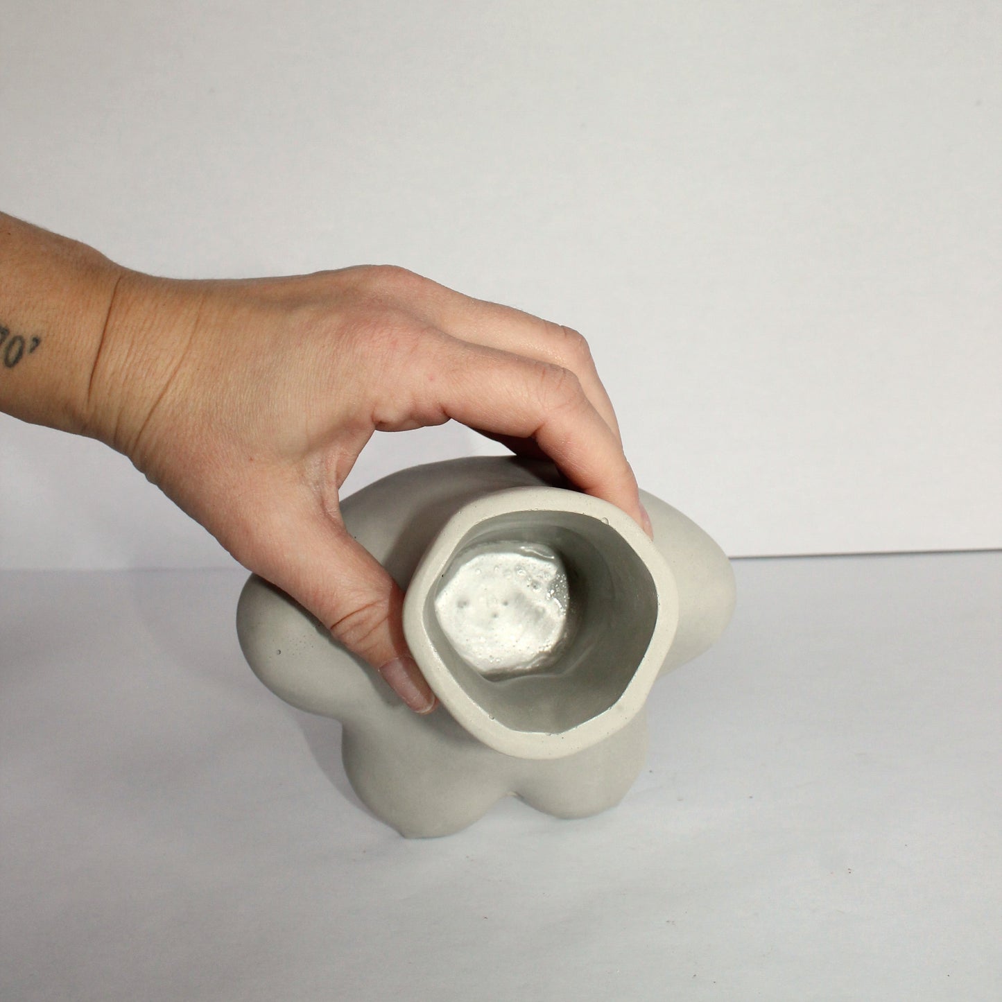 Hand holding a gray concrete flower vase against a white background