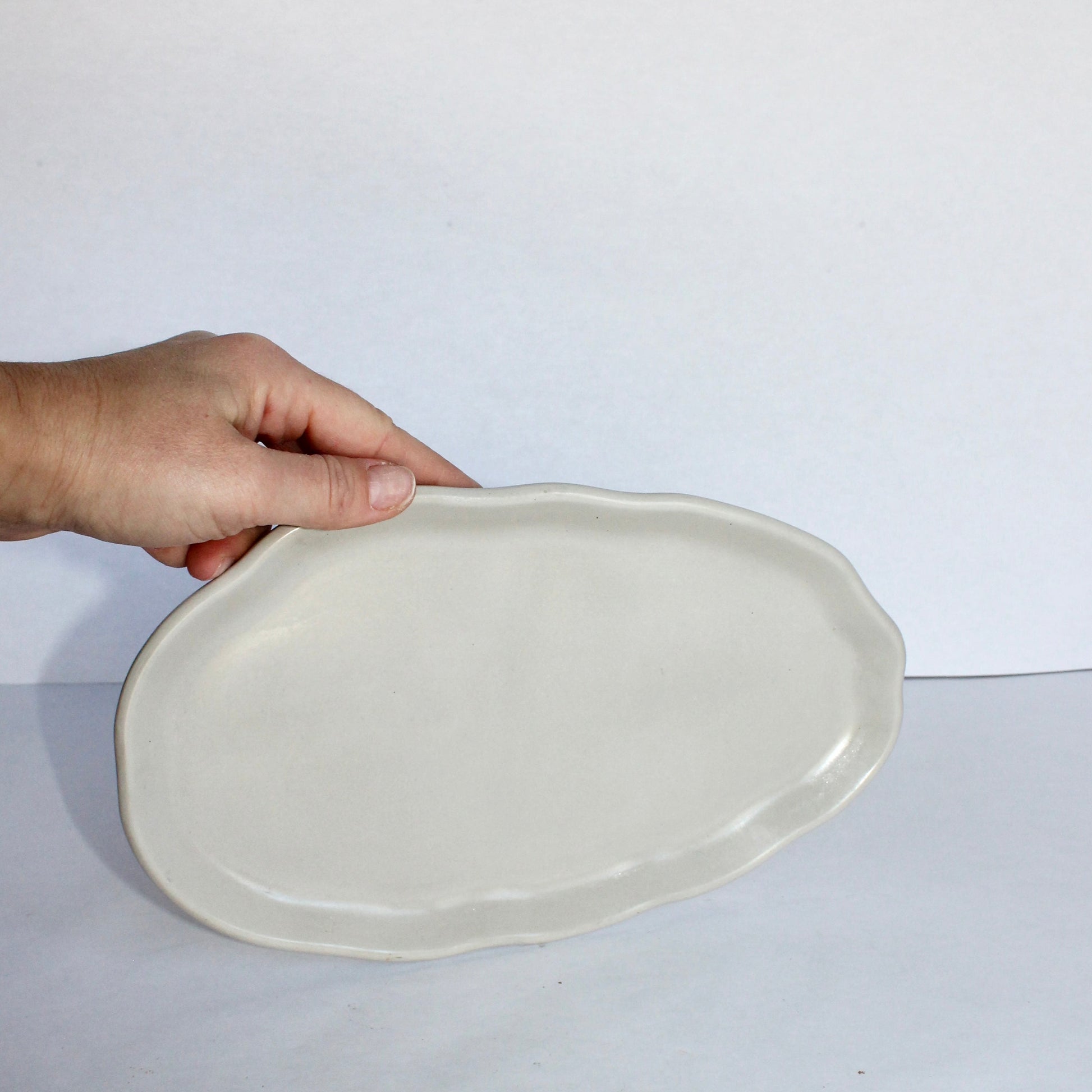 Hand holding a light gray ceramic plate against a white background