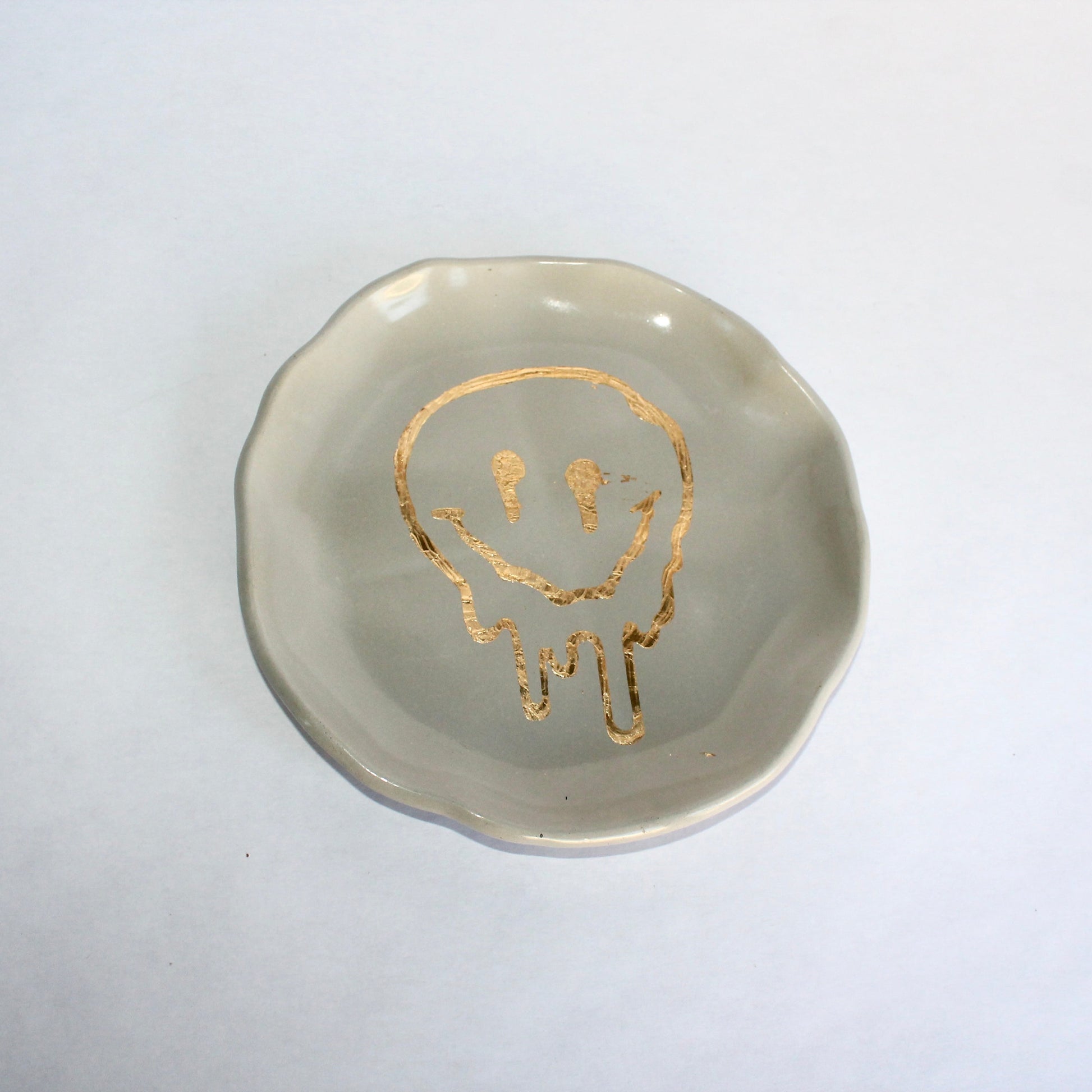 Round concrete dish with gold melting smiley face design on a white background