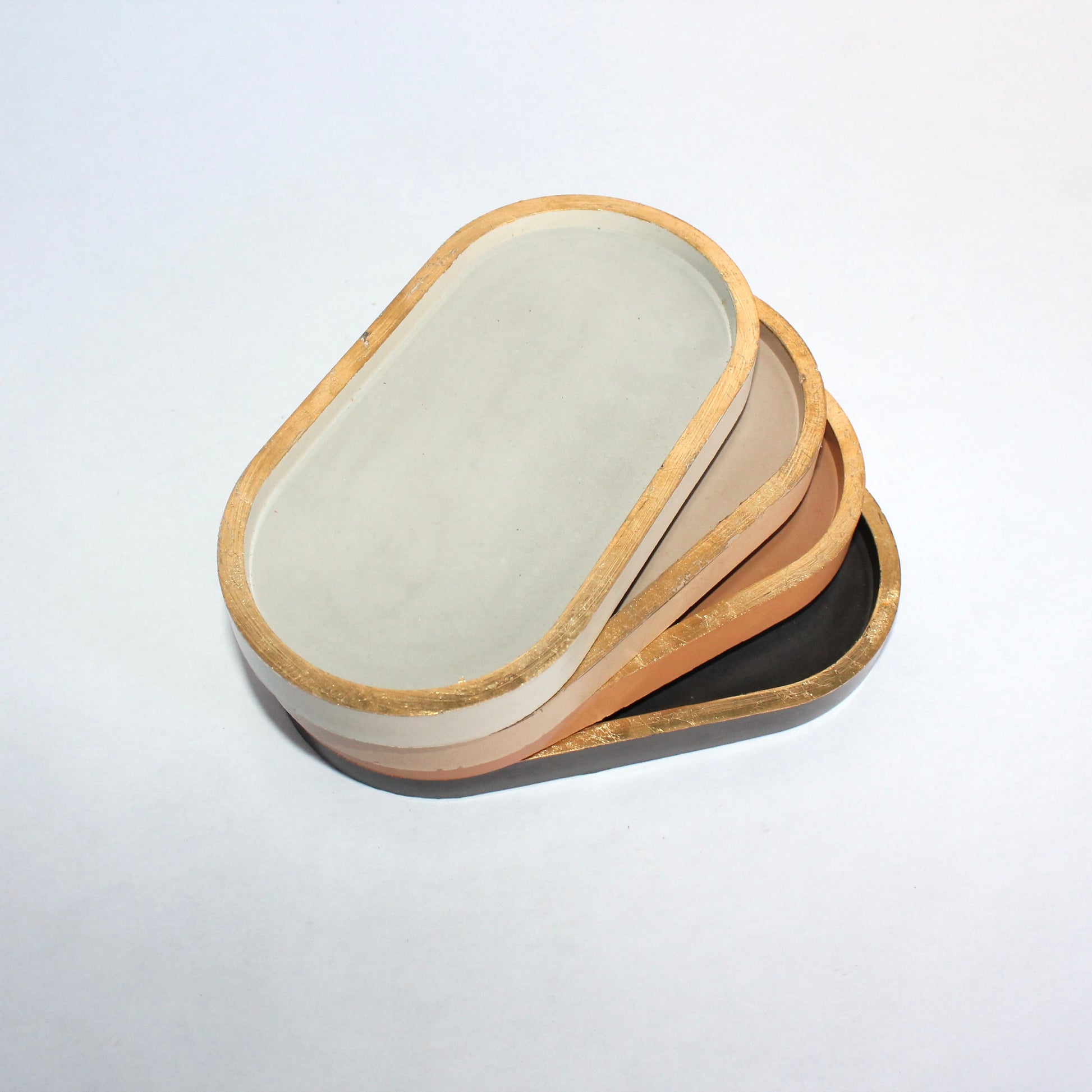 Stack of oval concrete dishes with gold rim on a white background