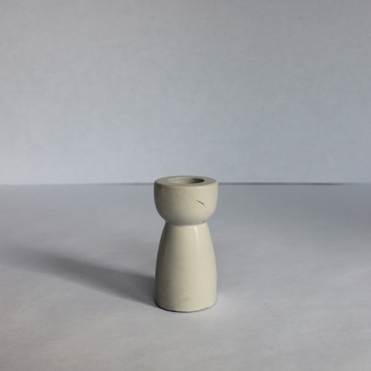 Small gray concrete candle stick holder on a white surface with a plain background
