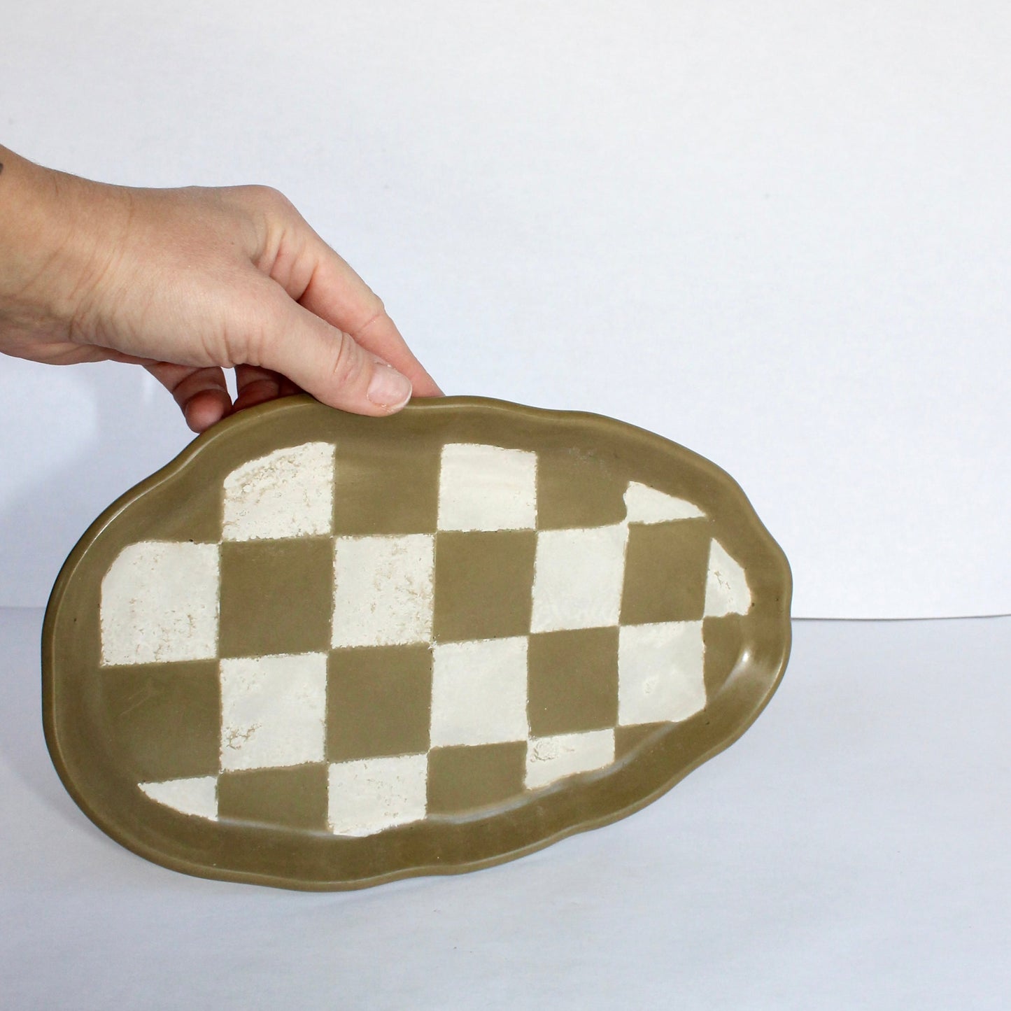 Hand holding a green concrete dish with a checkered pattern on a white background