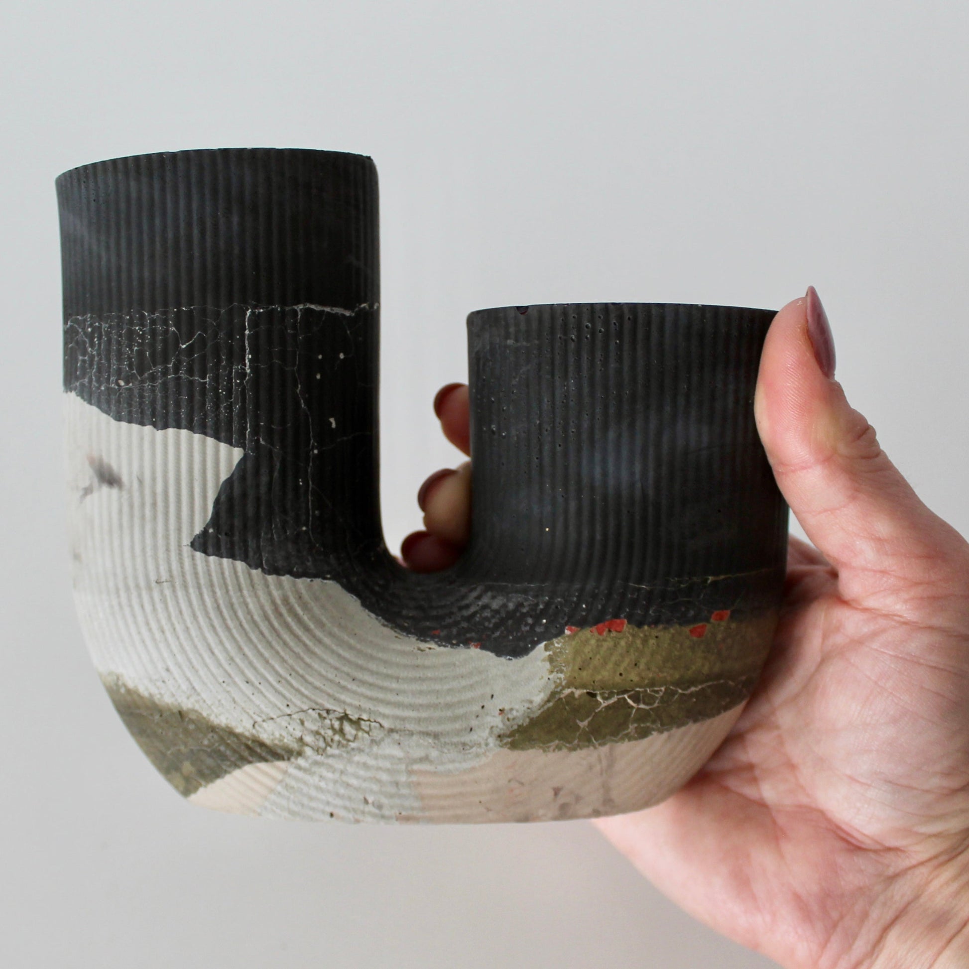 Hand holding a black and white cement vase against a plain background