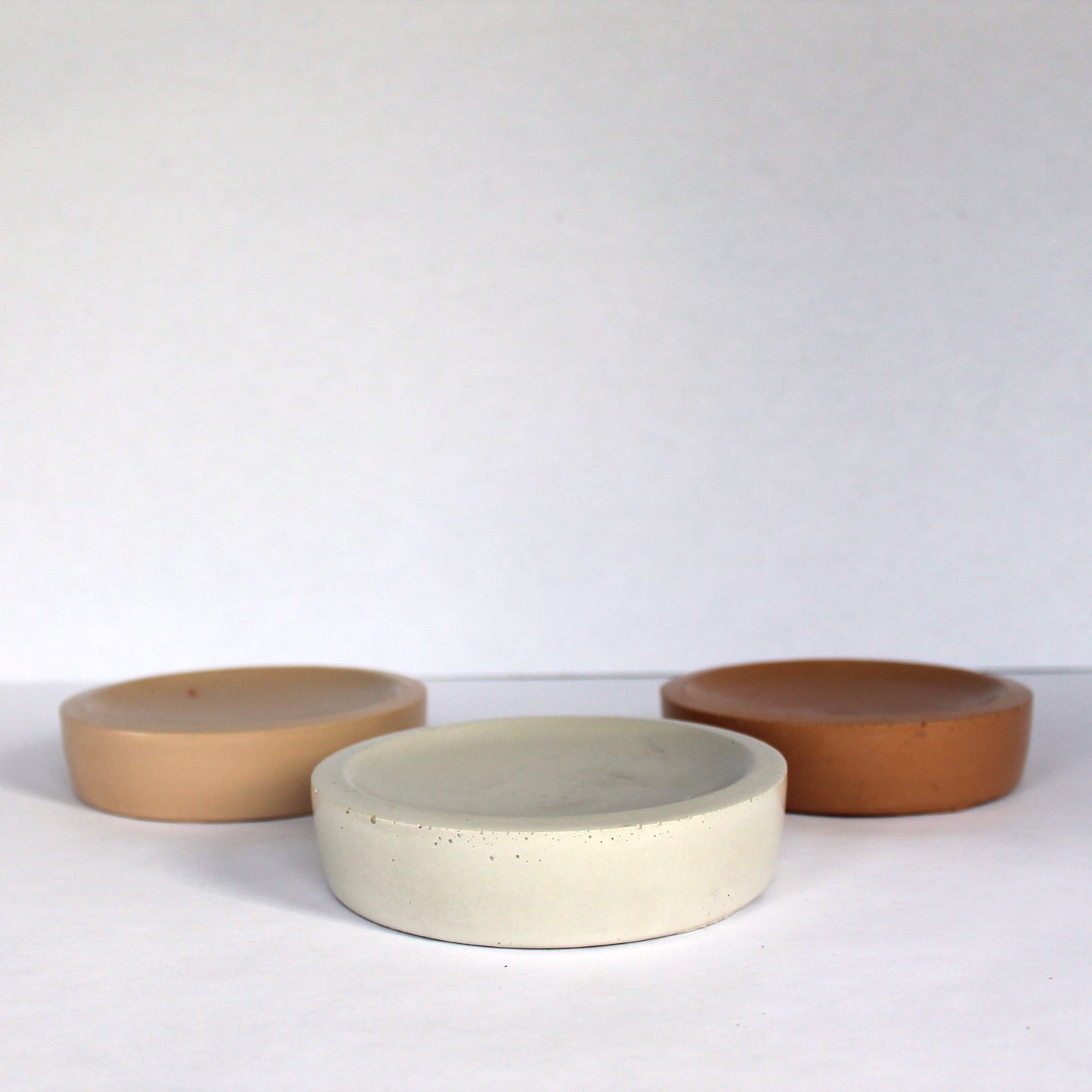 Three neutral concrete bowls in beige, brown, and white on a white background
