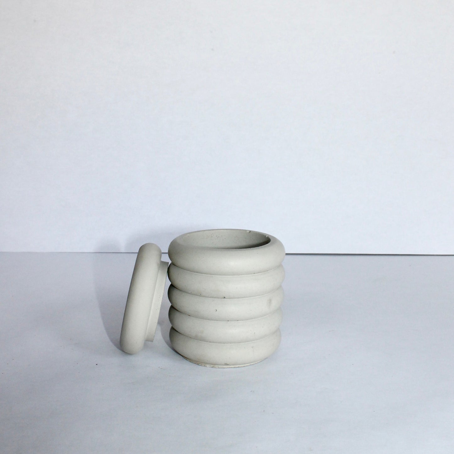 light gray concrete jar with lid propped on the side on a white background