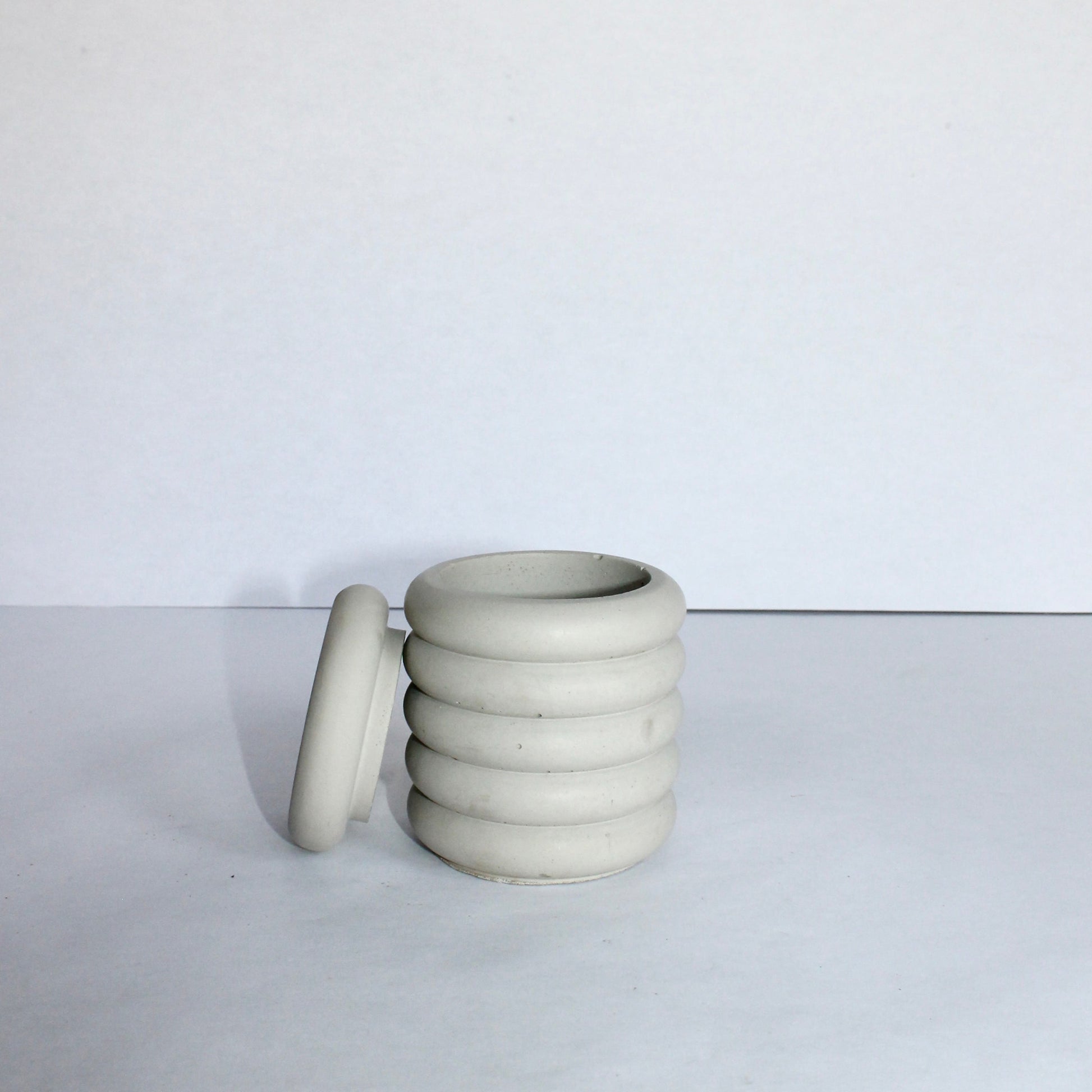 light gray concrete jar with lid propped on the side on a white background
