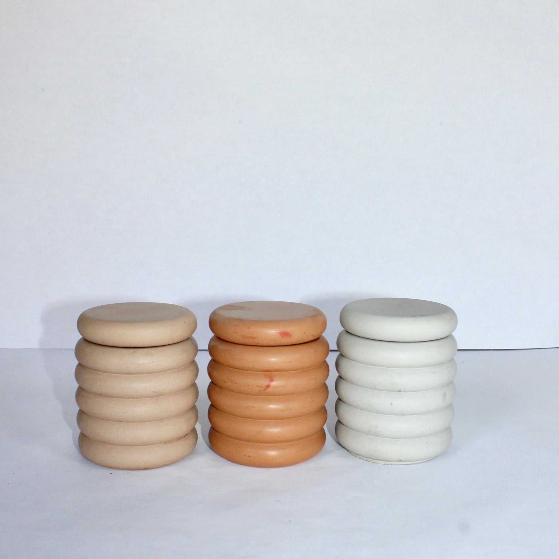 Three concrete jars in beige, terracotta, and light gray on a white surface with a white background