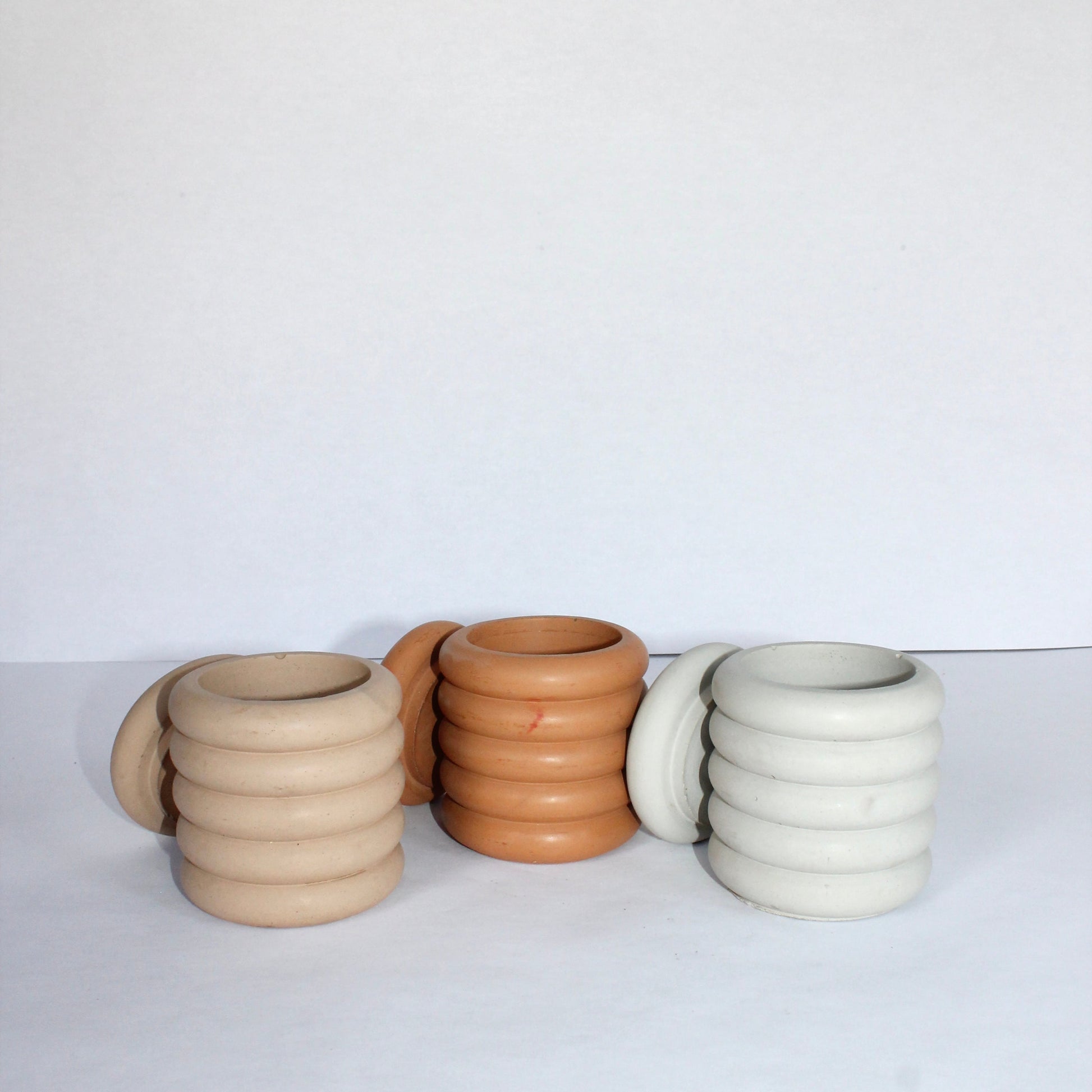 Four concrete jars with lids in different neutral colors on a white background