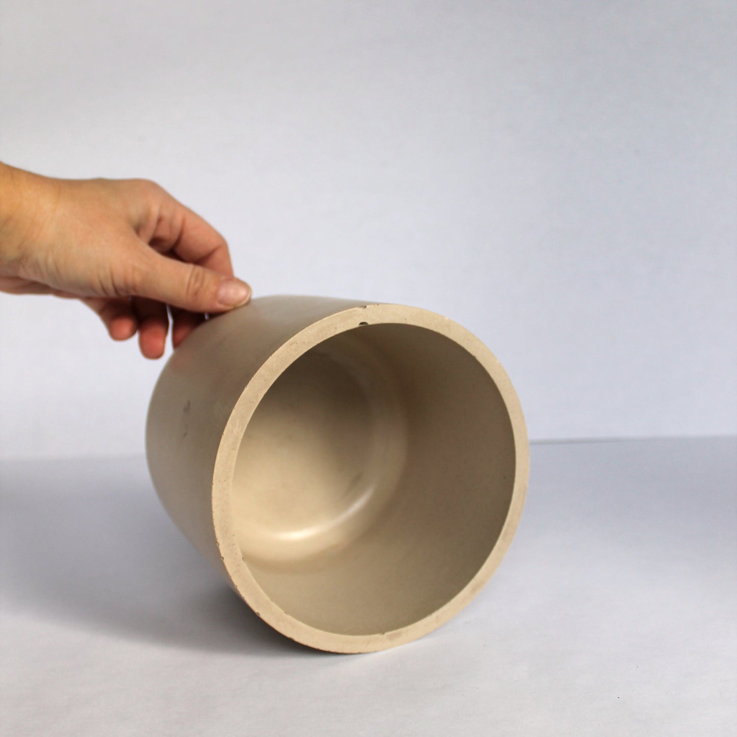 Hand holding a beige concrete pot on a white background