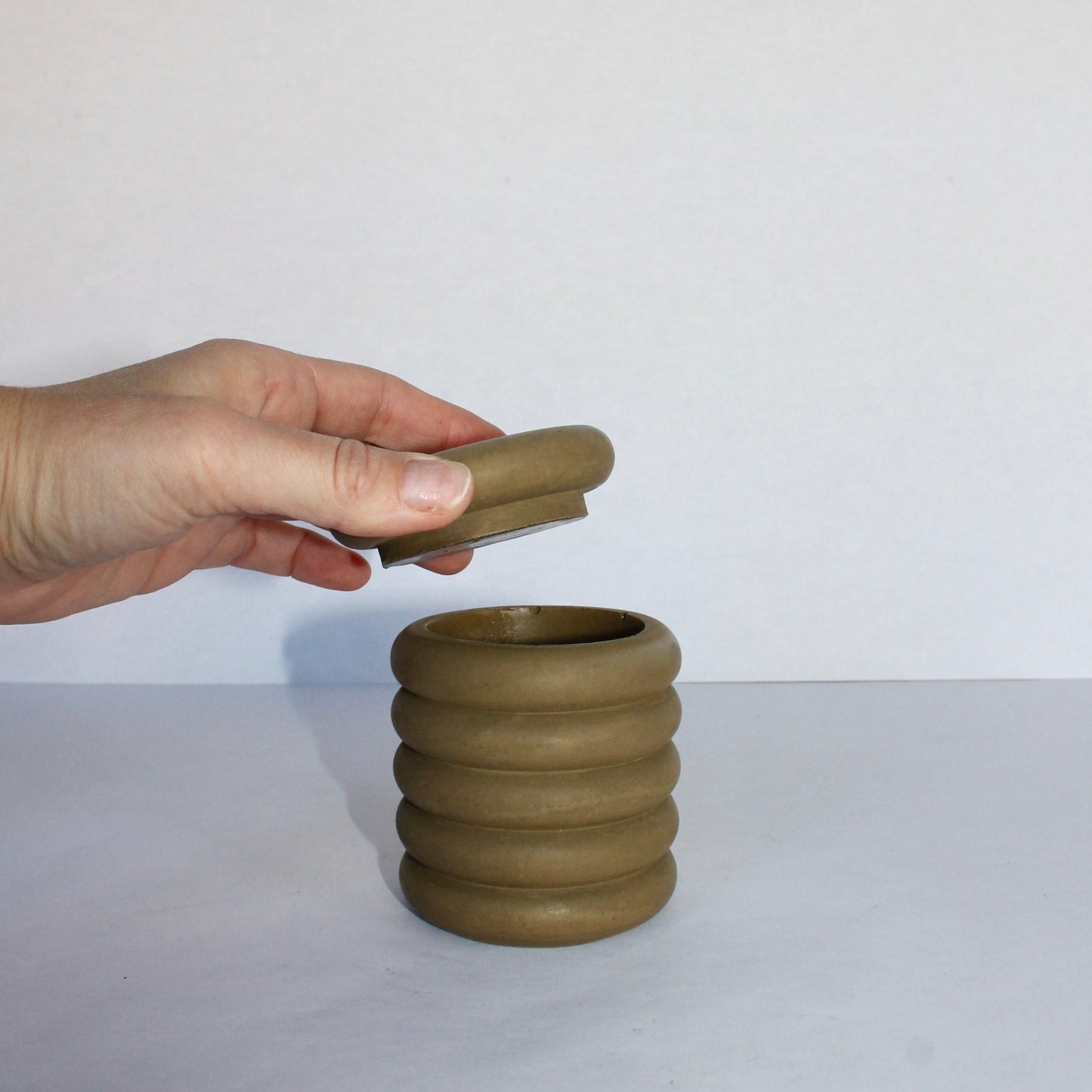 Hand holding a green lid over a matching concrete container on a white background