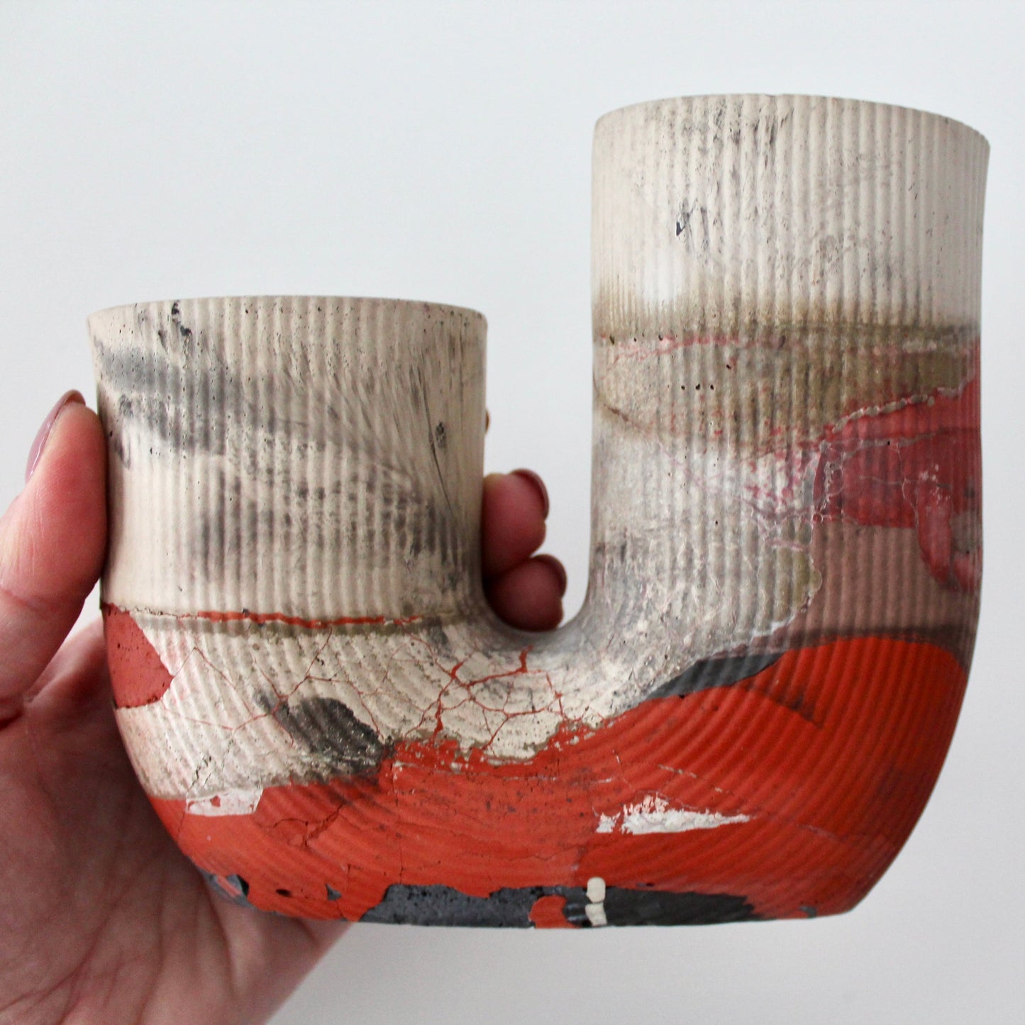 Hand holding a J-shaped object with textured surface and red and orange accents on a white background