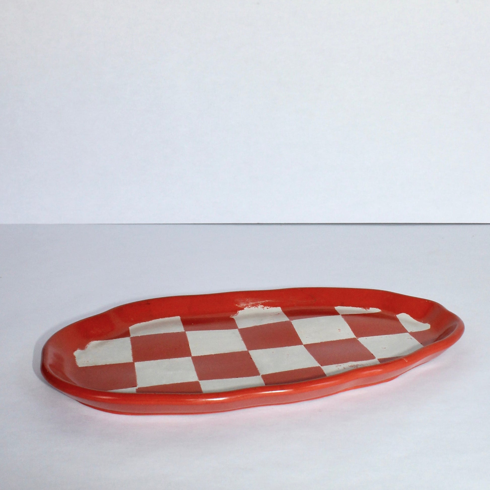 Checkered orange and light gray oval ceramic plate on a white background