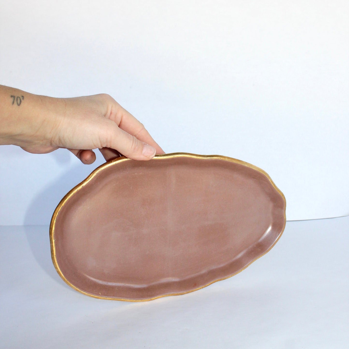 Hand holding a brown concrete tray with gold rim on a white background