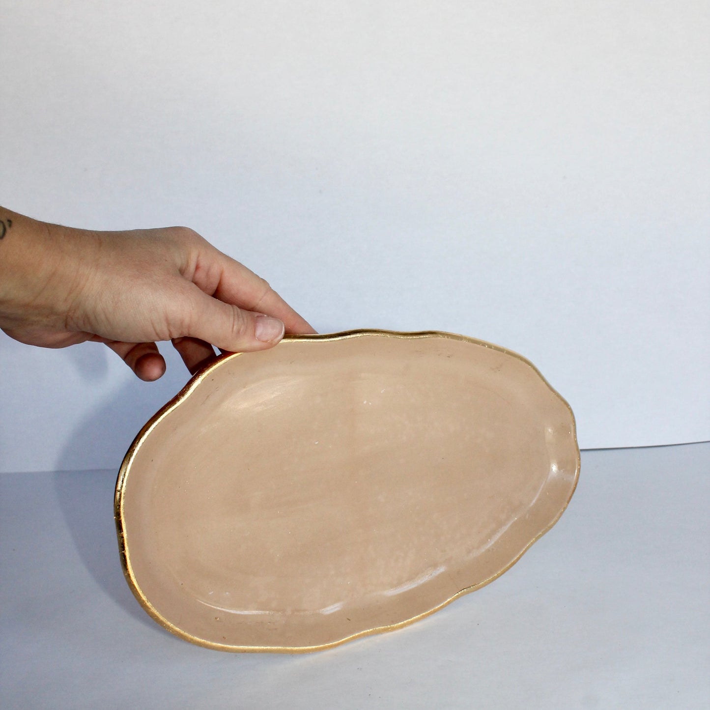 Hand holding a beige concrete plate with gold rim against a white background
