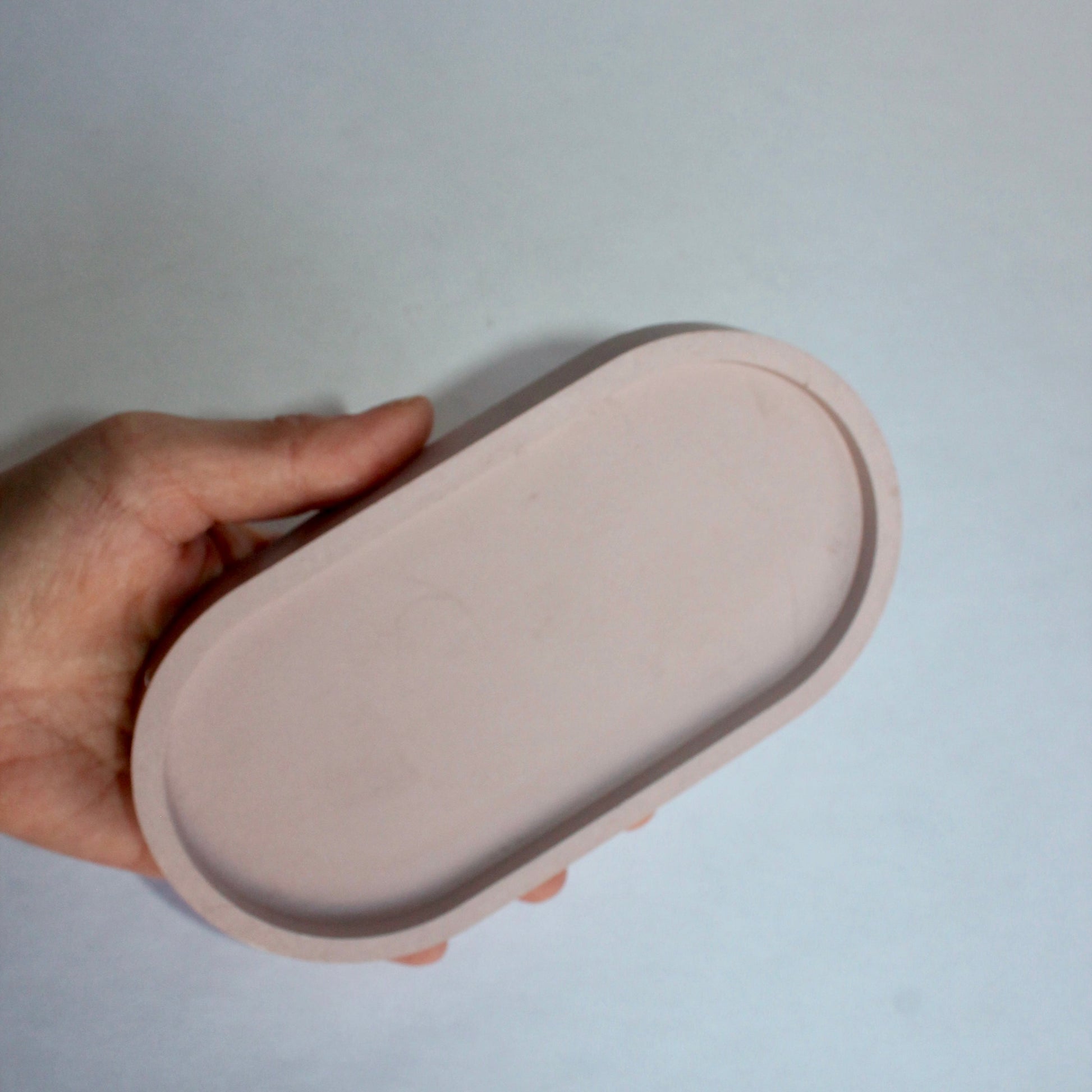 Hand holding a pale pink oval tray against a white background