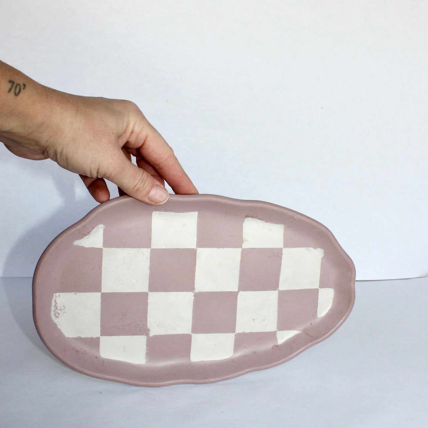 Hand holding a pink and white checkered cement tray against a white background