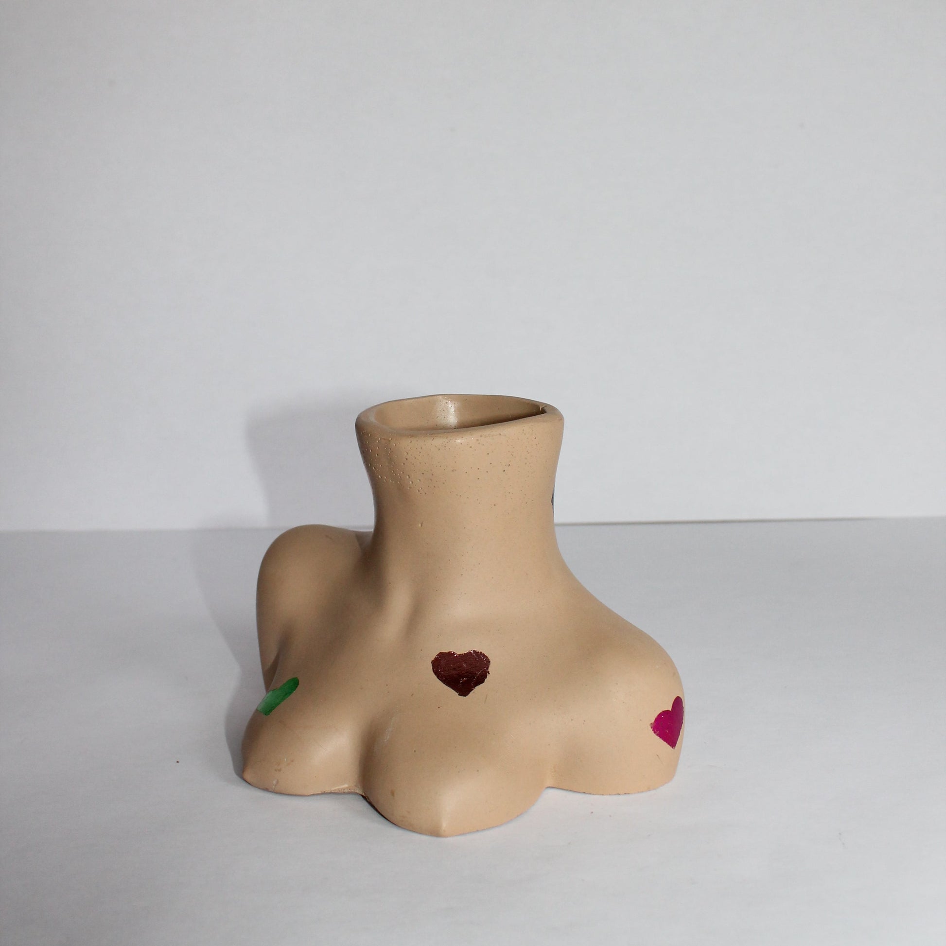 Vase shaped like a beige female torso with a heart detail on a plain background