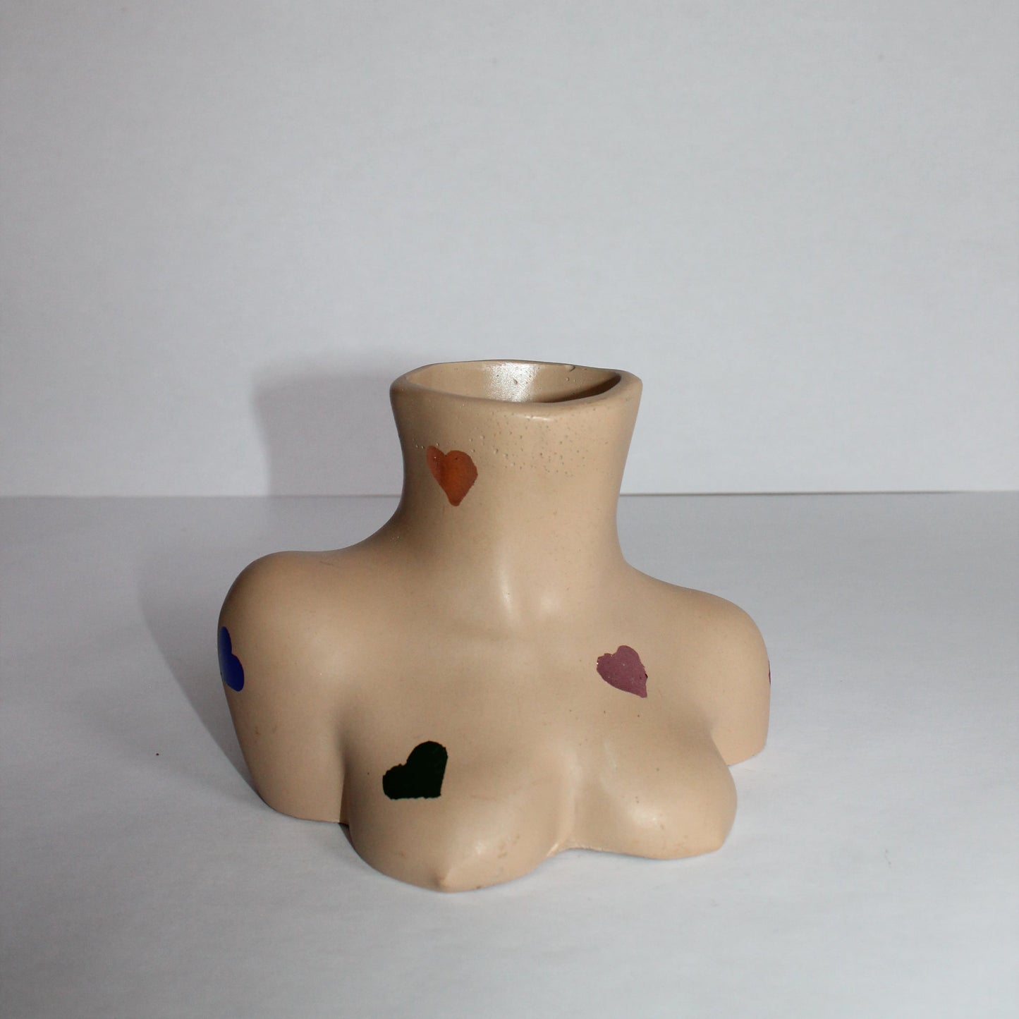 Ceramic breast-shaped vase with colorful hearts on a white background