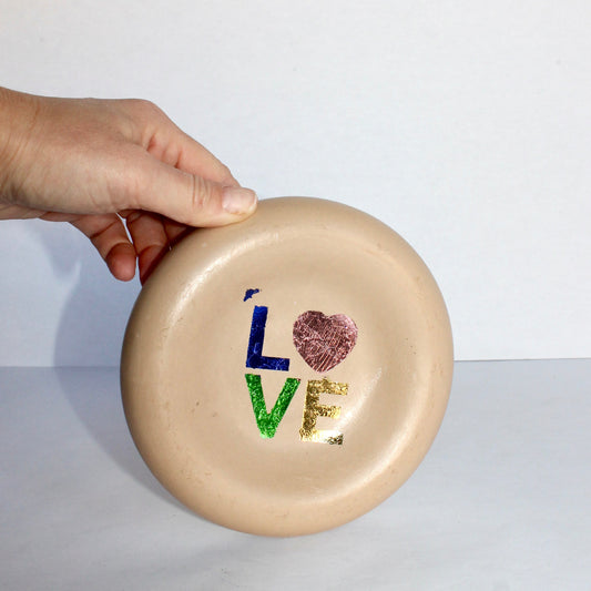 Hand holding a beige concrete tray with 'LOVE' and heart design on a white background