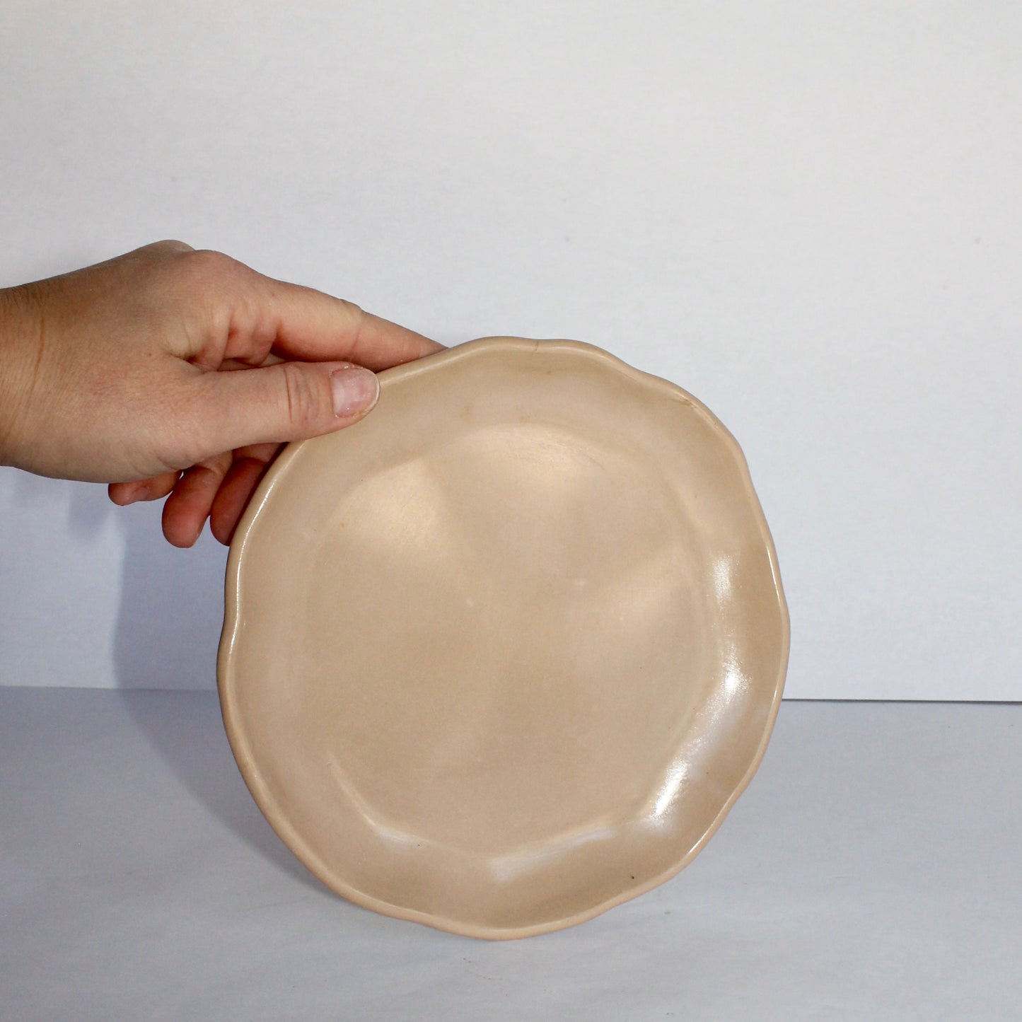 Beige concrete plate held by a hand against a white background