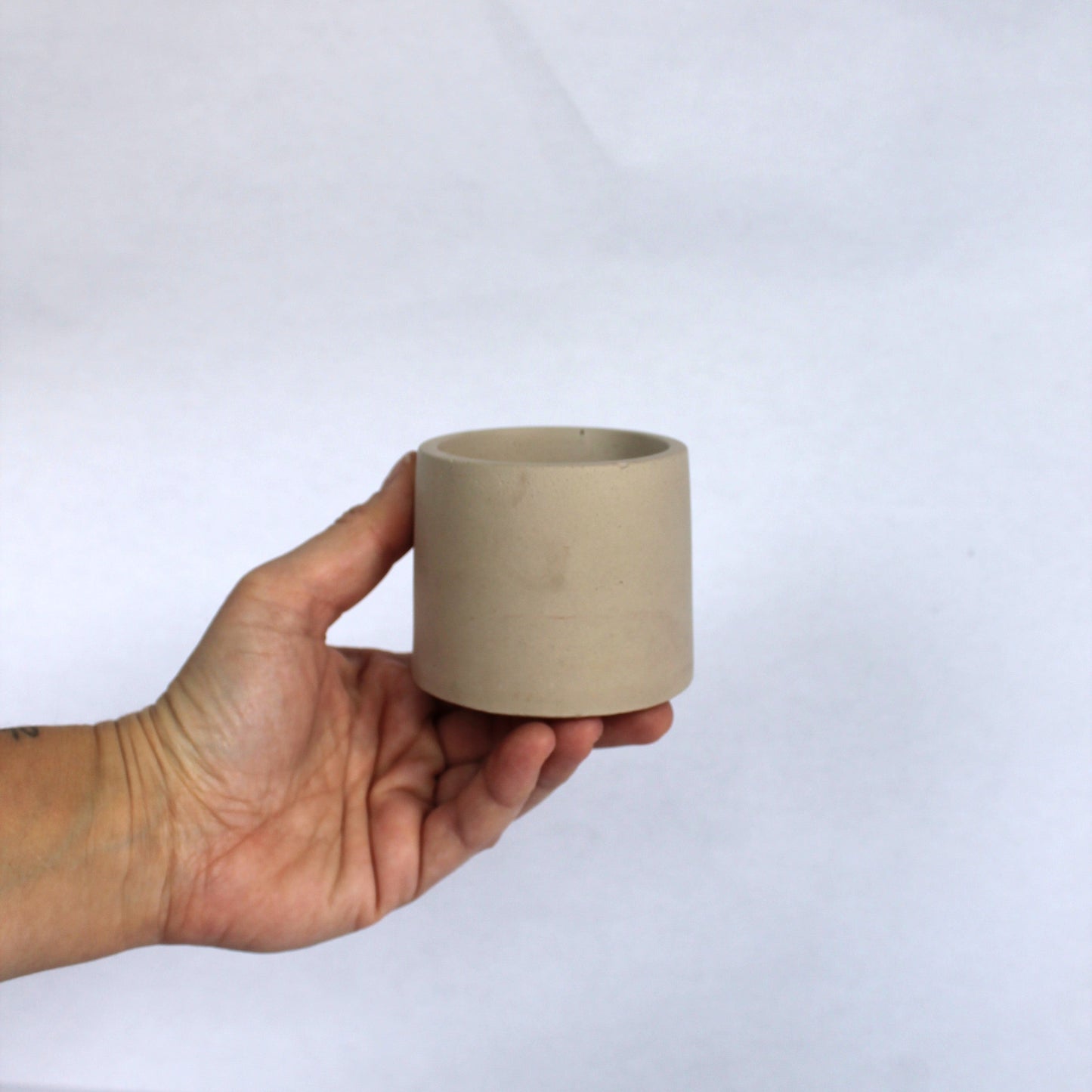 Hand holding a beige concrete pot against a white background