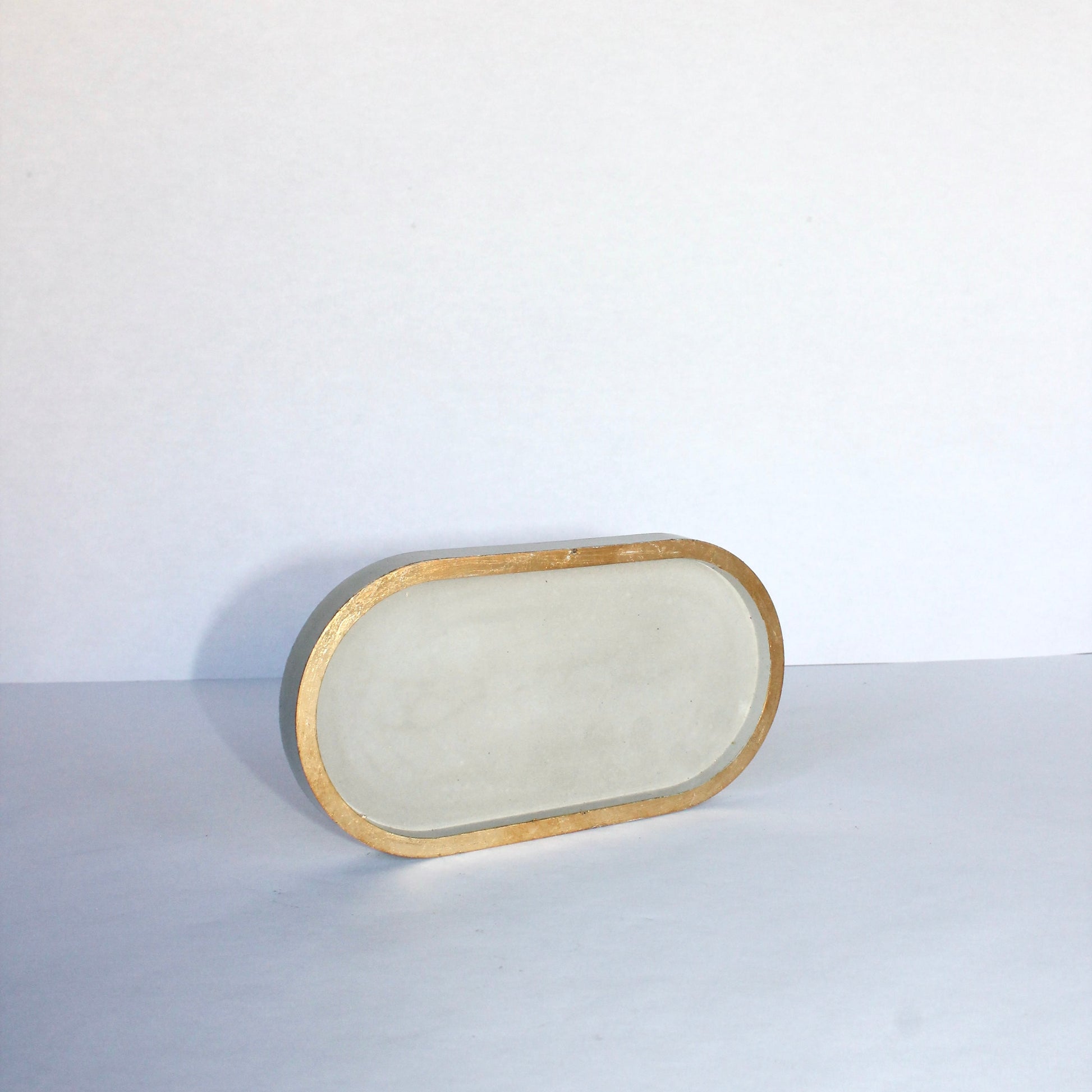 light gray small oval tray with gold edge on a white background