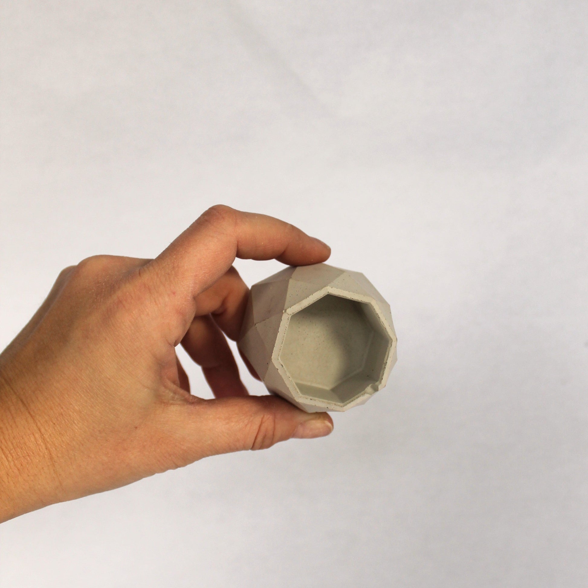 Hand holding a small geometric concrete object against a plain background