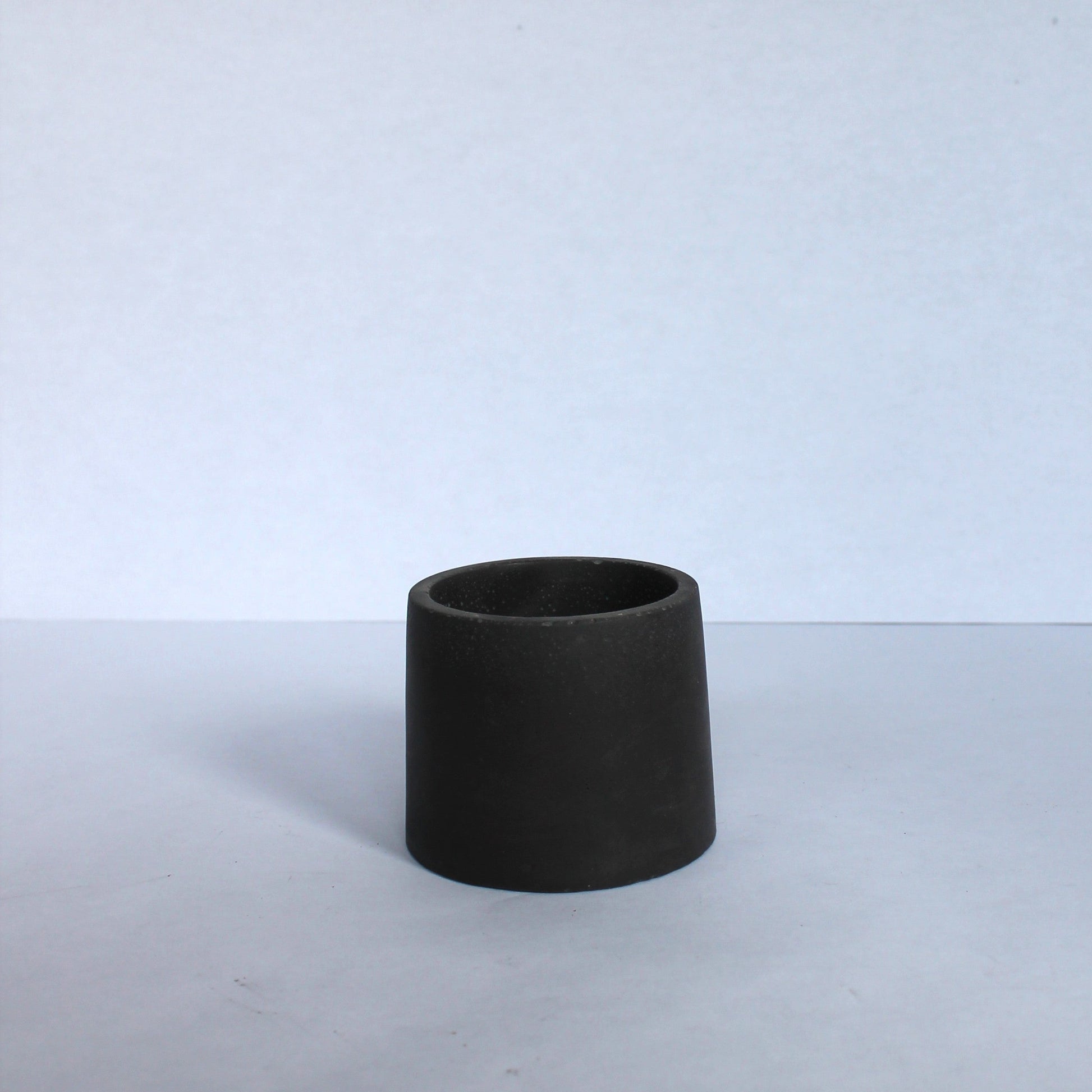 Black concrete cylindrical pot on a white surface and background