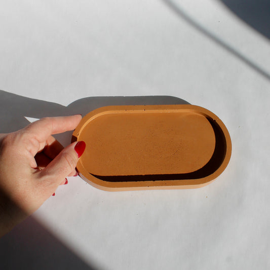 hand holding a terracotta colored concrete oval tray on a white background