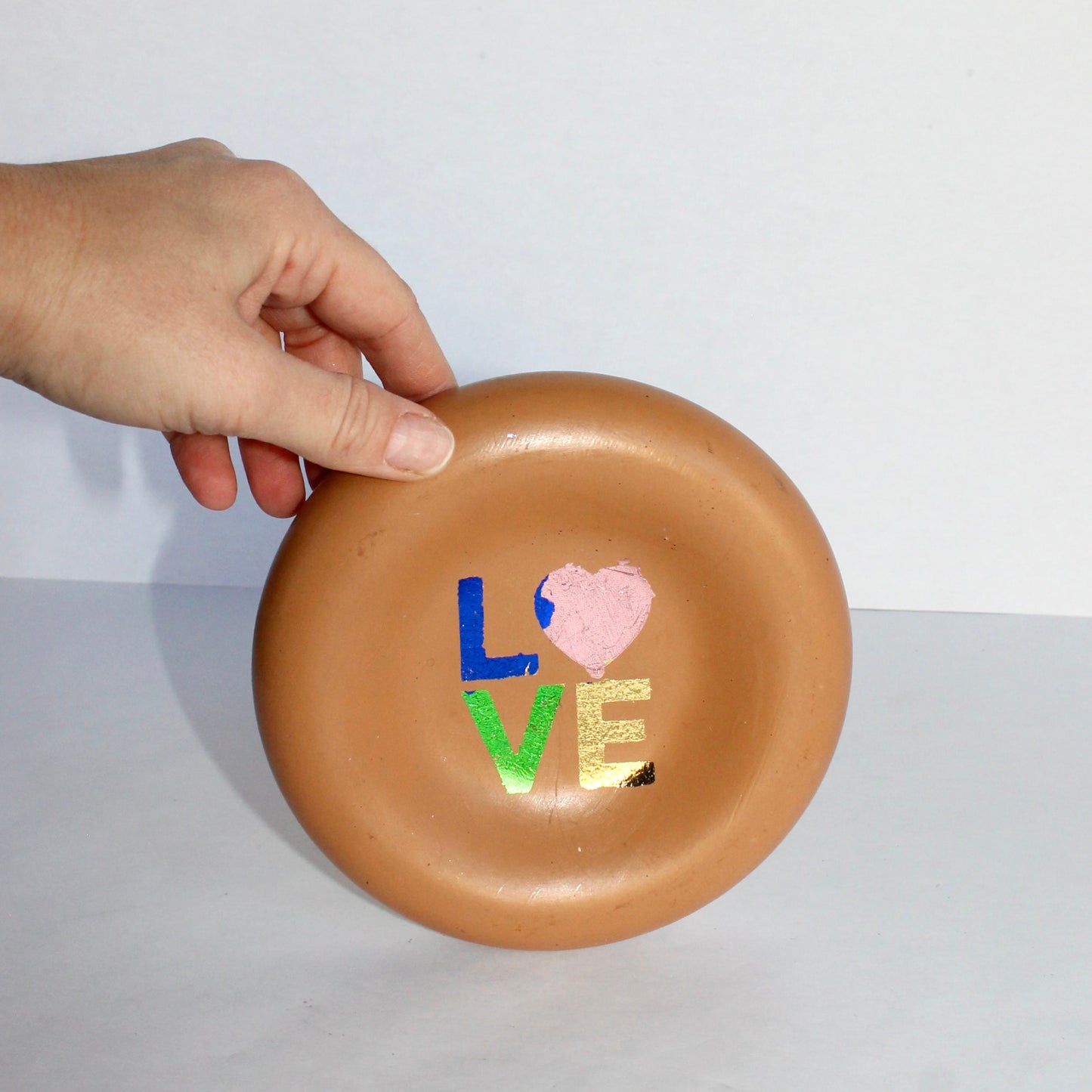 thick round concrete tray with 'LOVE' and heart design held by a hand on a white background