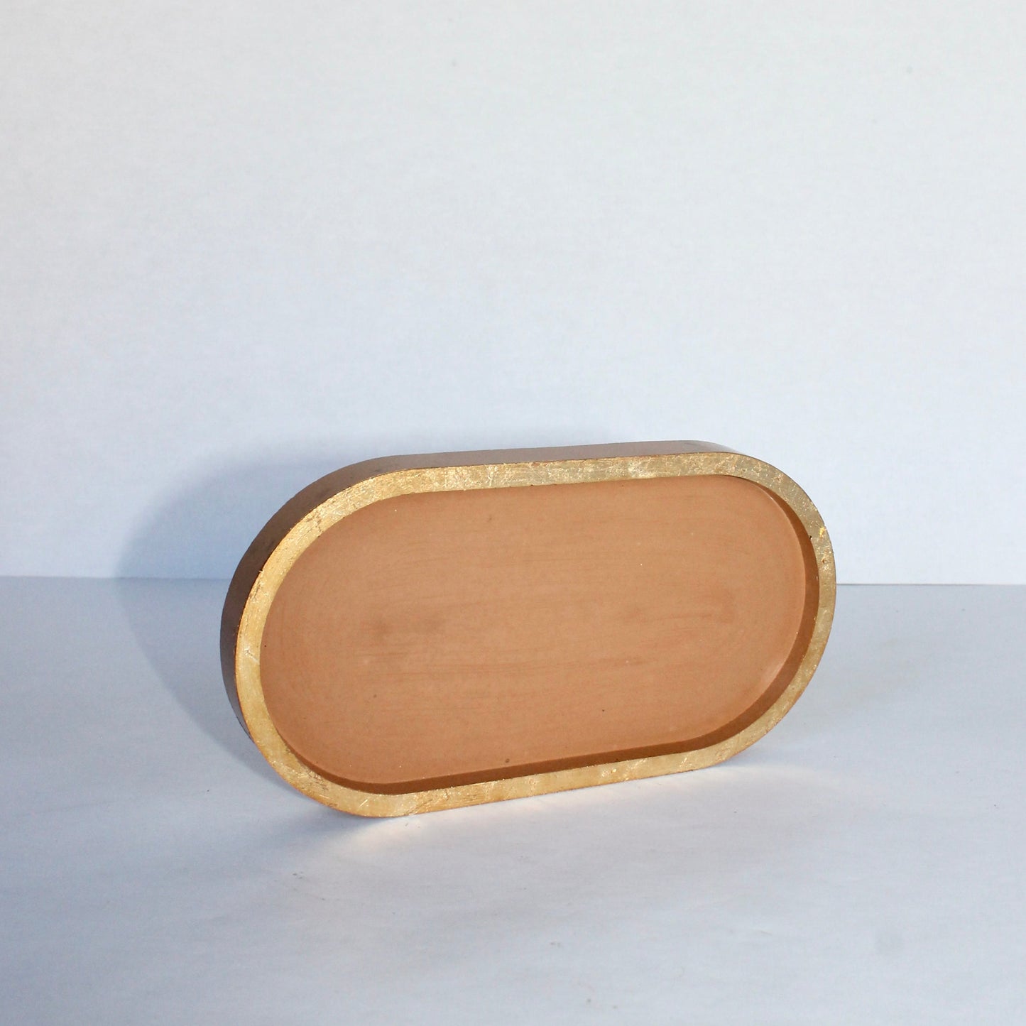 Terracotta colored concrete tray with gold rim on a white background