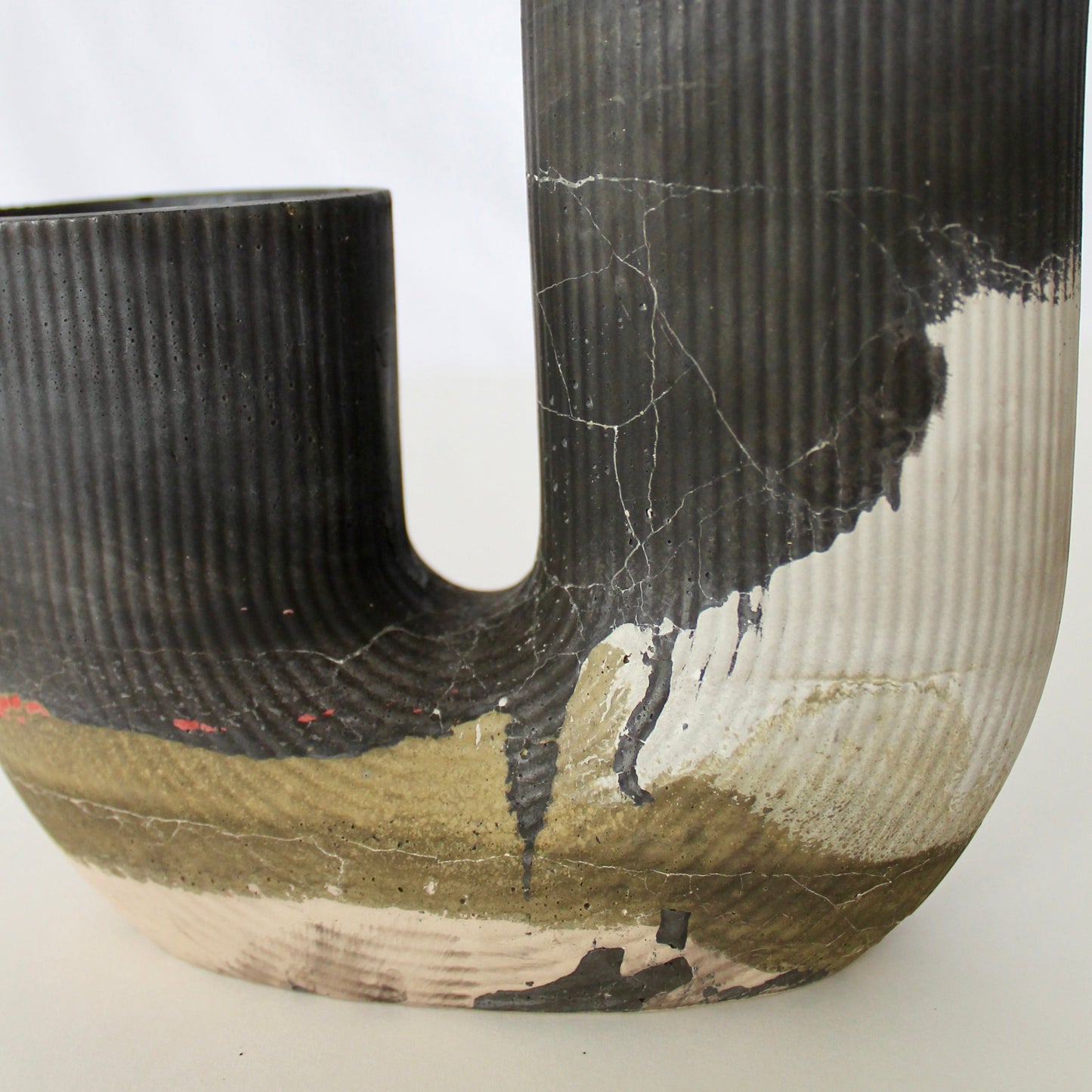 J shaped concrete vase with two openings, with textured surfaces on a white background
