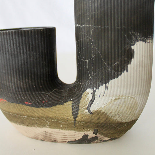 J shaped concrete vase with two openings, with textured surfaces on a white background