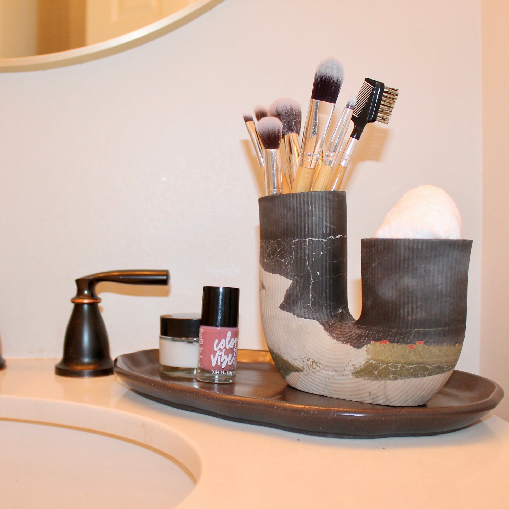 Bathroom sink with toiletries and a decorative vase holding makeup brushes.