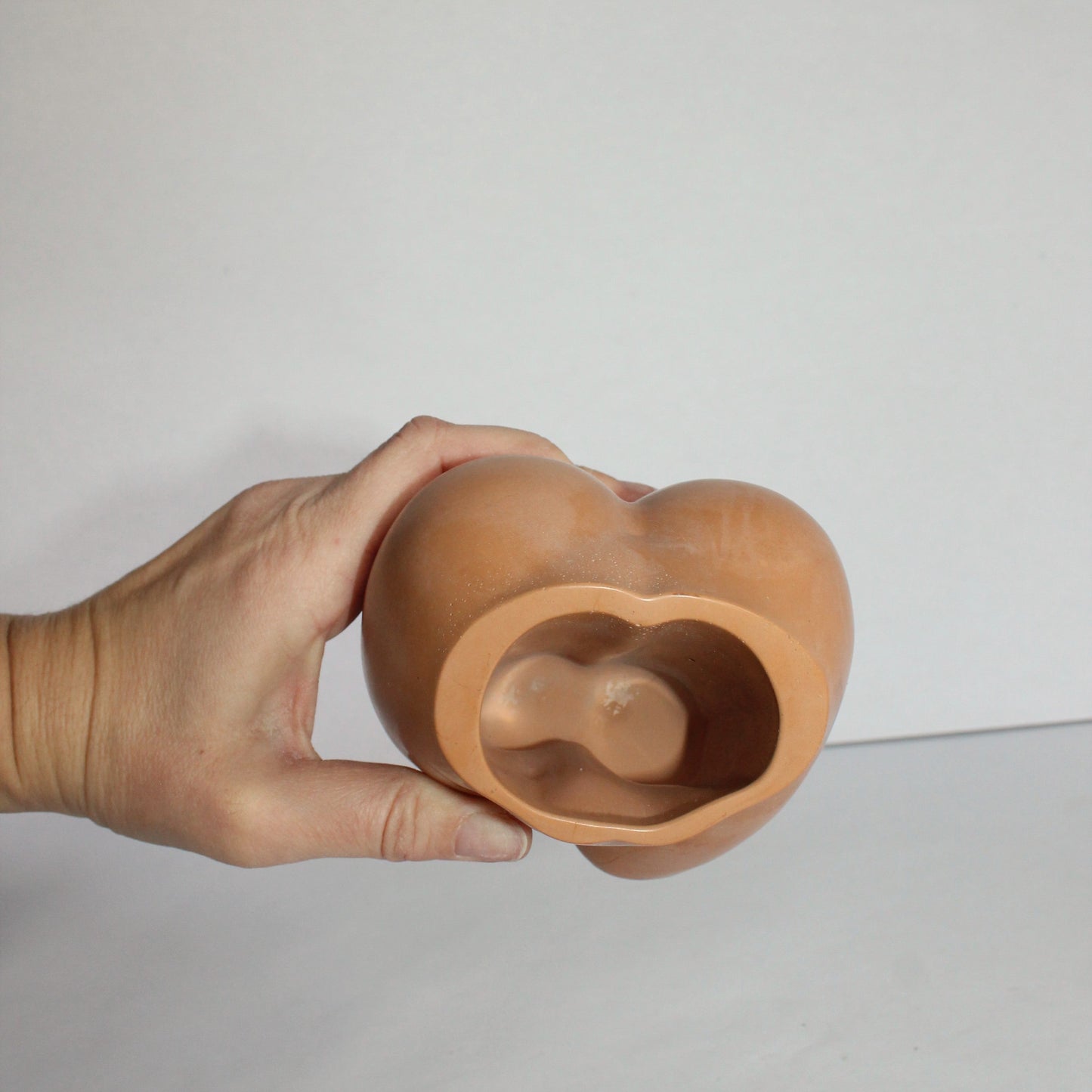 Hand holding a terracotta ceramic object against a plain background